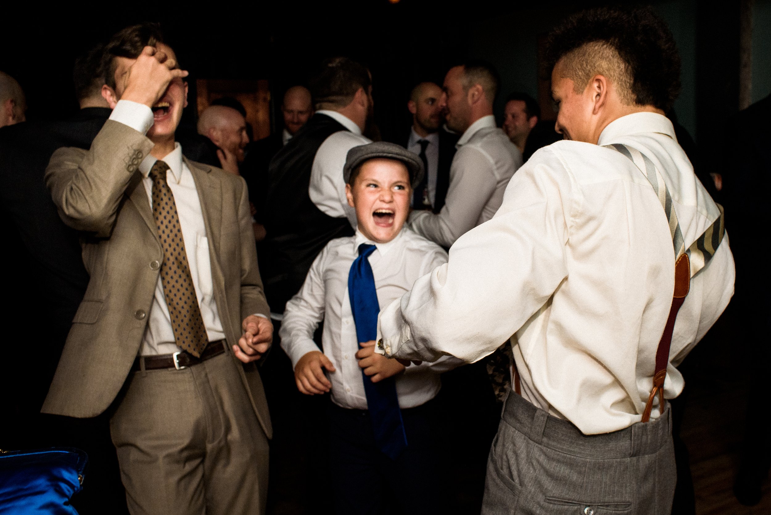 three young men in suits and tie laughing and dancing in dark room illuminated by flash