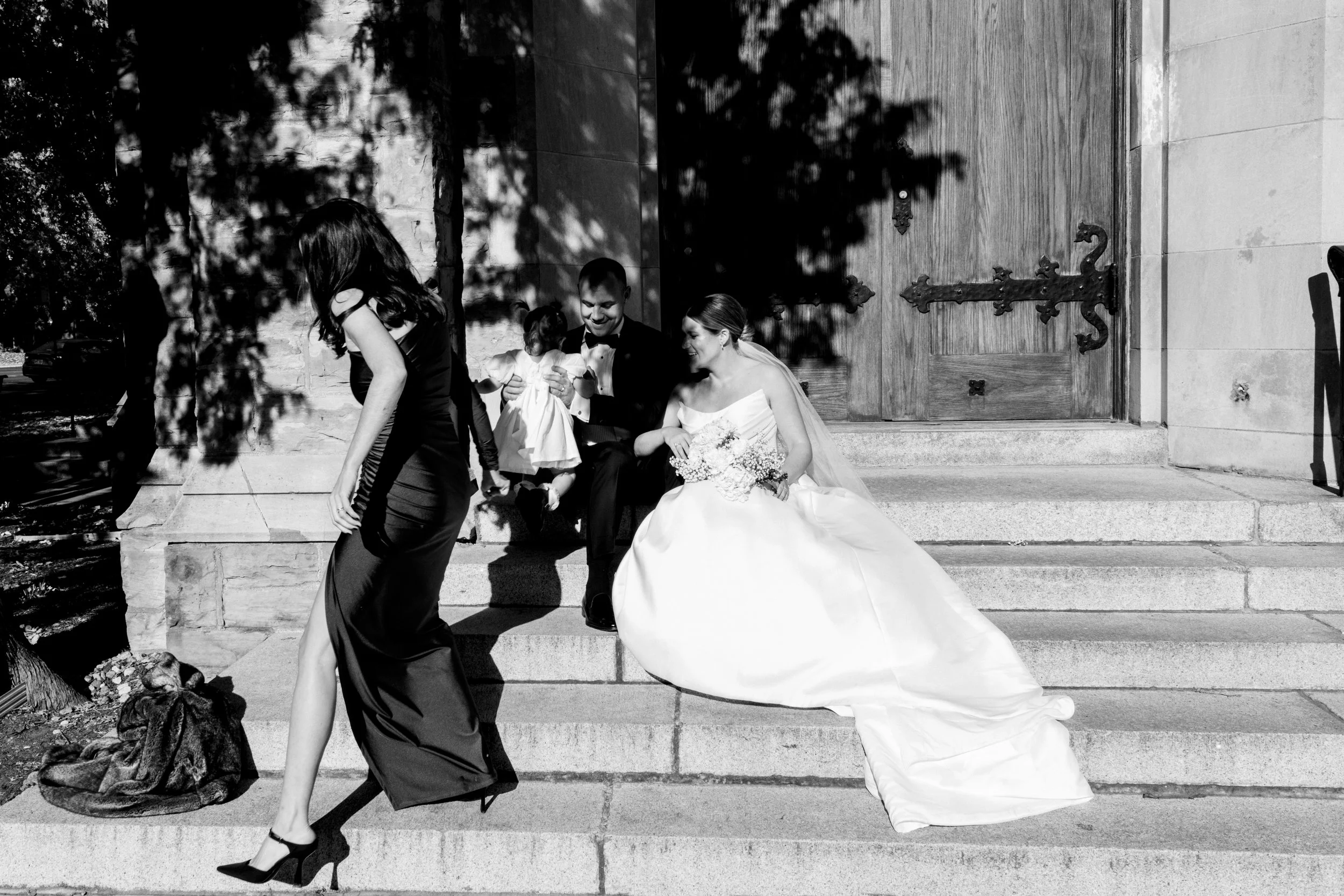BTS Black and white wedding photo of a bridesmaid walking out of frame after handing a toddler to a Montreal bride and groom.