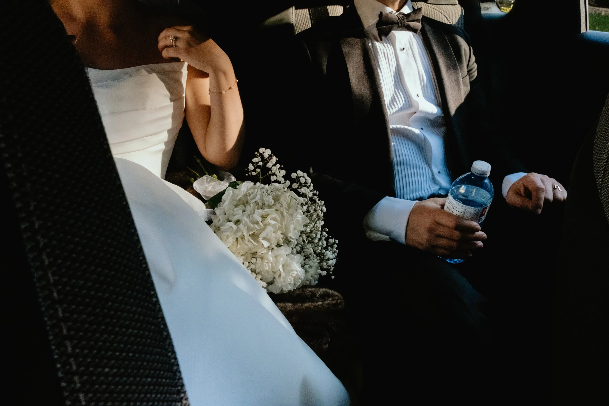 Close-up of a Montreal bride and groom inside a limousine after the ceremony, with the bride adjusting her dress and the groom holding a water bottle.