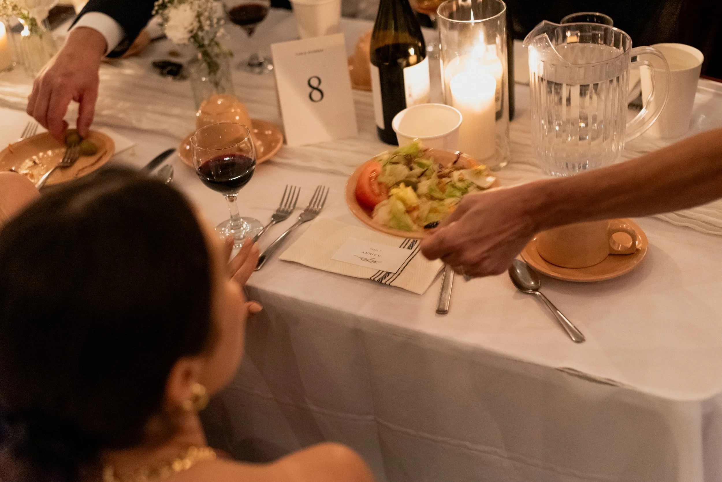 Candid documentary-style photo of Chalet BBQ dinner service at a Montreal wedding, with a woman serving salad while a guest's hand reaches for an olive.