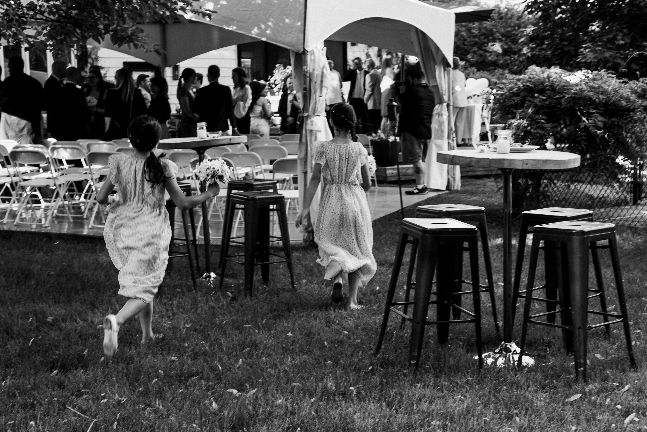 two young girls in dresses run across grassy area of backyard wedding