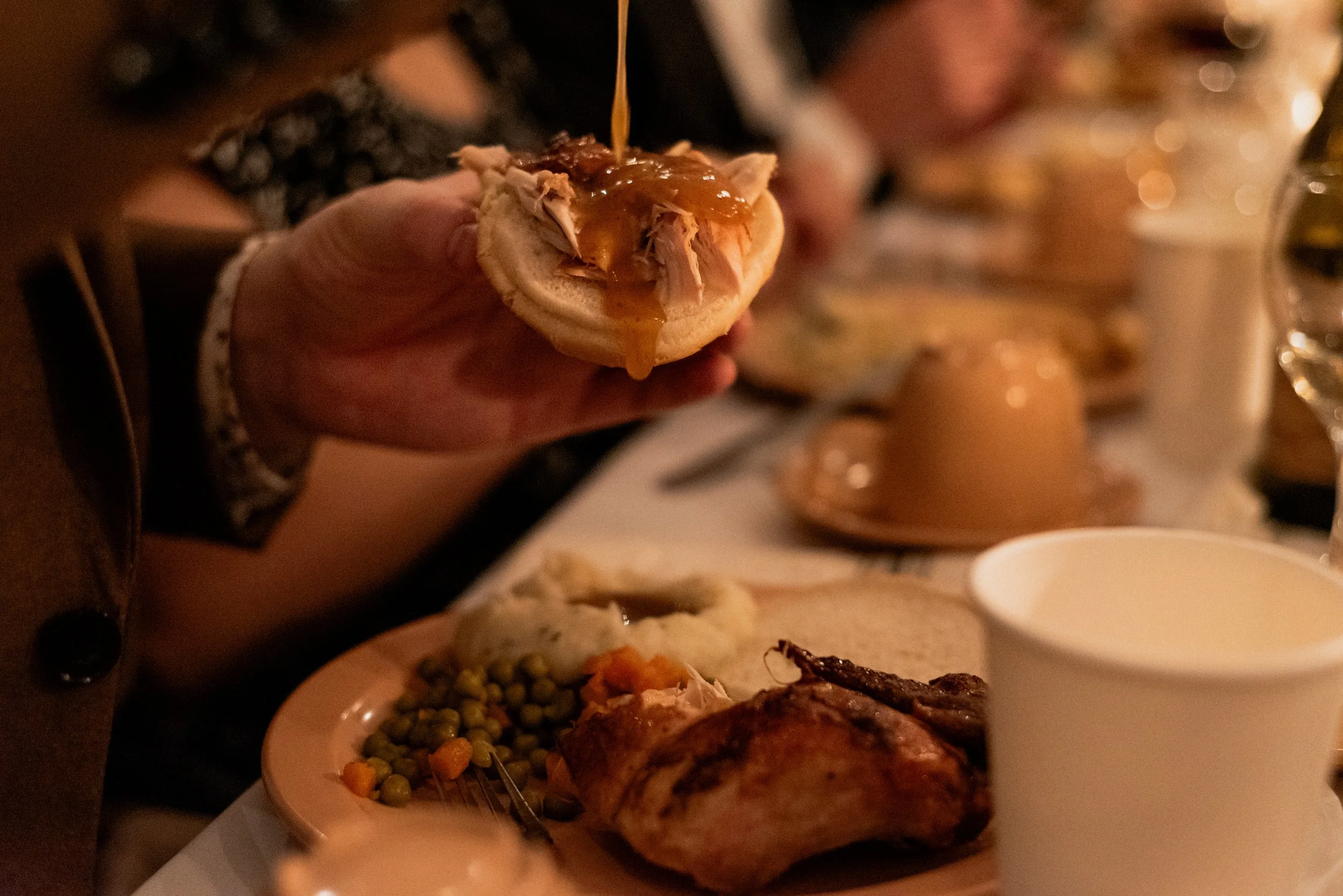 Candid documentary-style photo of Chalet BBQ dinner service at a Montreal wedding, with a guest drizzling bbq sauce over a chicken sandwich in soft warm candlelight