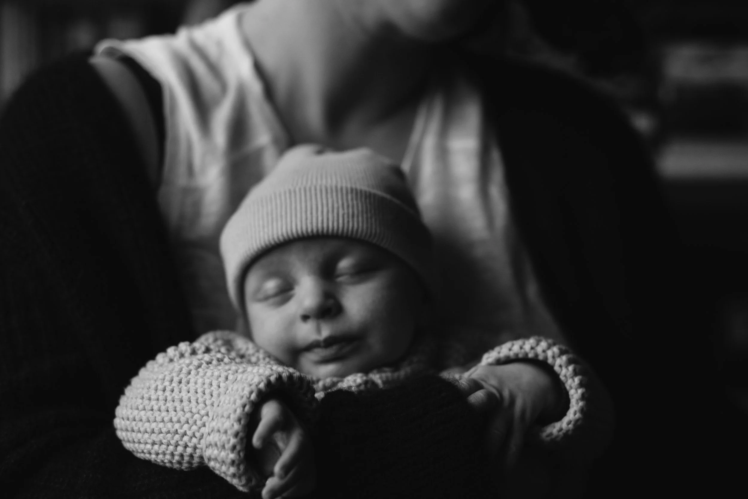 A black and white photo of a sleeping infant being cradled by someone.