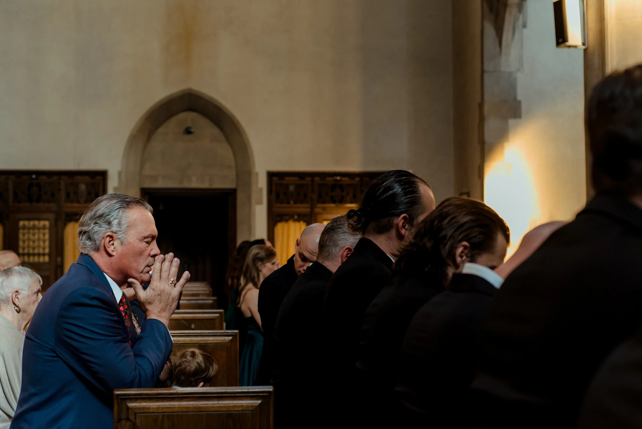 Man in navy suit kneeling at Montreal church pew in prayer