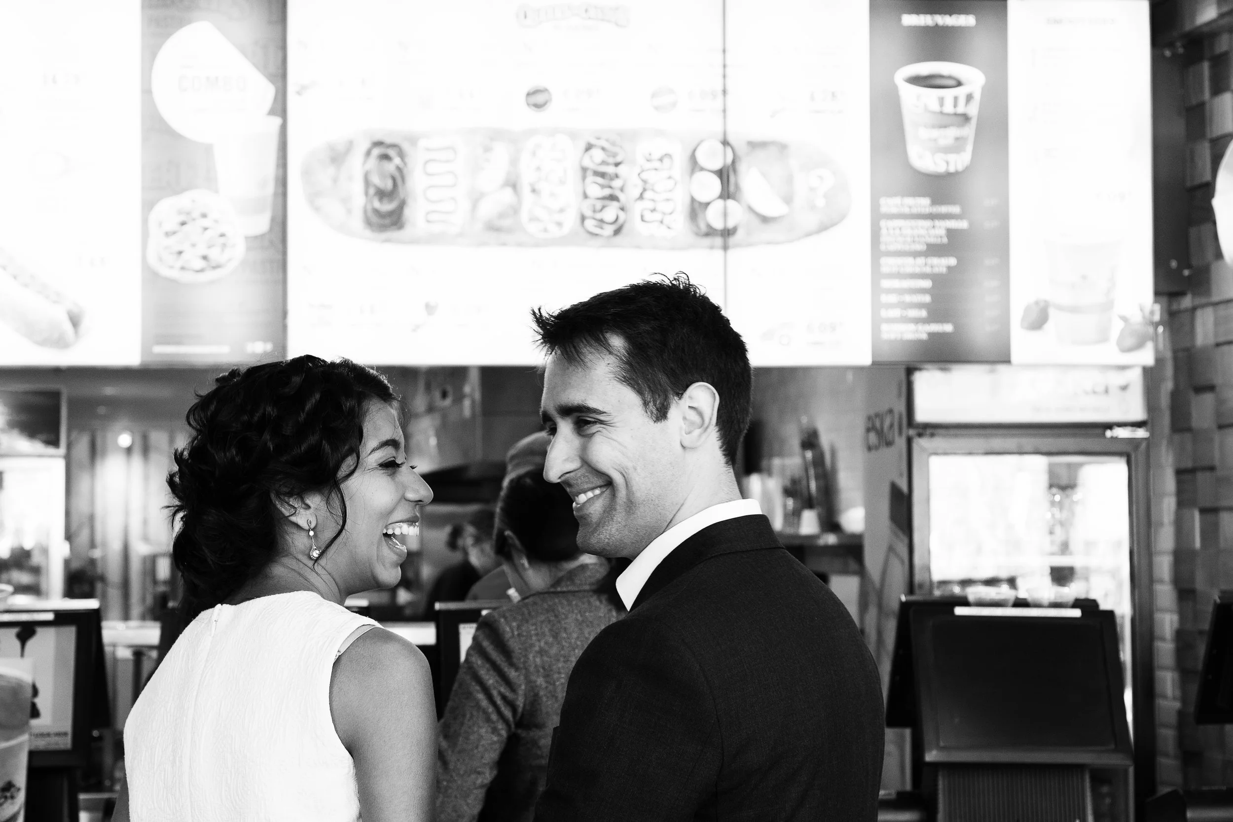 Bride and groom laughing, queueing at beaver tail store in wedding attire