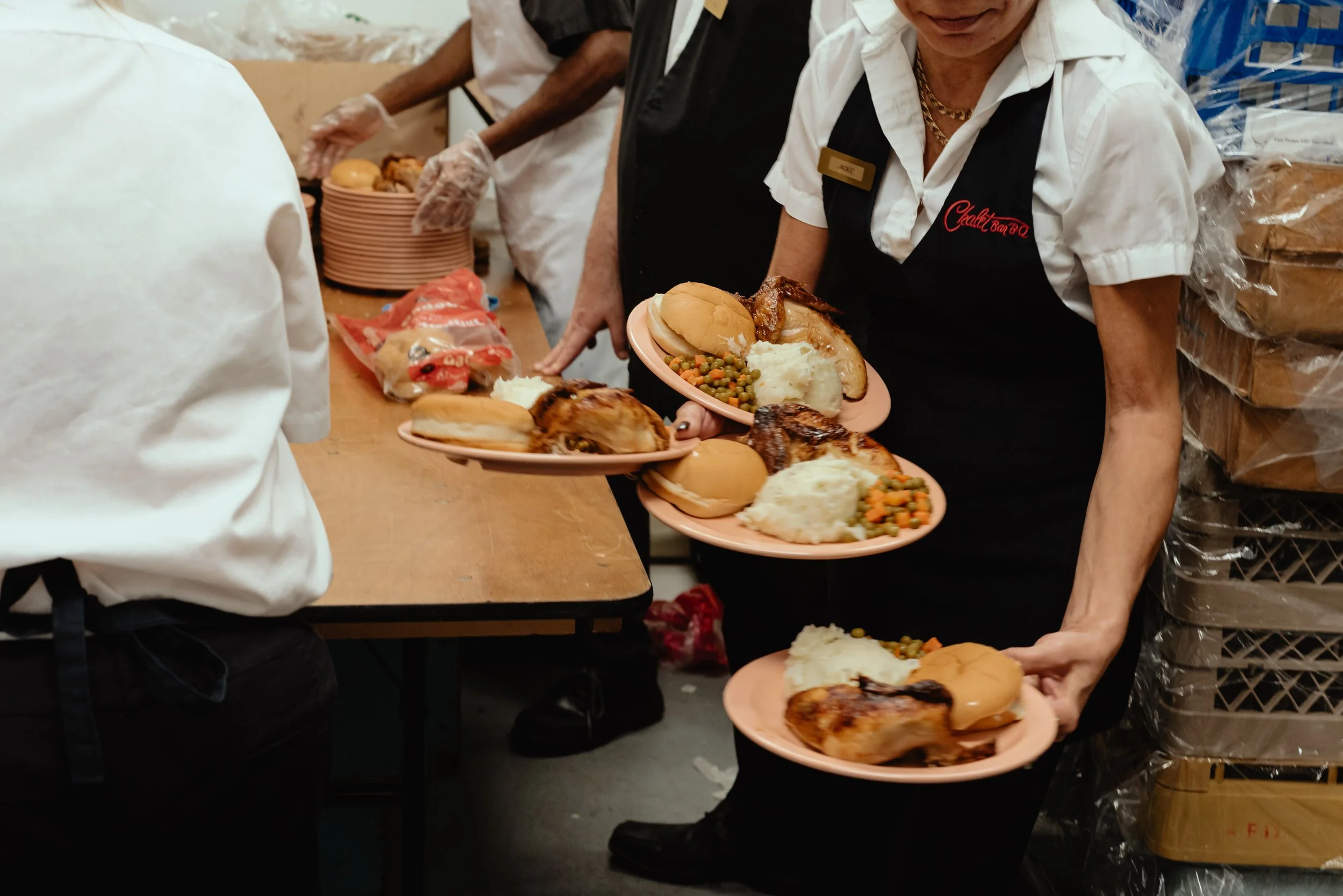 Candid documentary-style photo of Chalet BBQ dinner service at a Montreal wedding, with a server walking towards camera holding four dinner plates.
