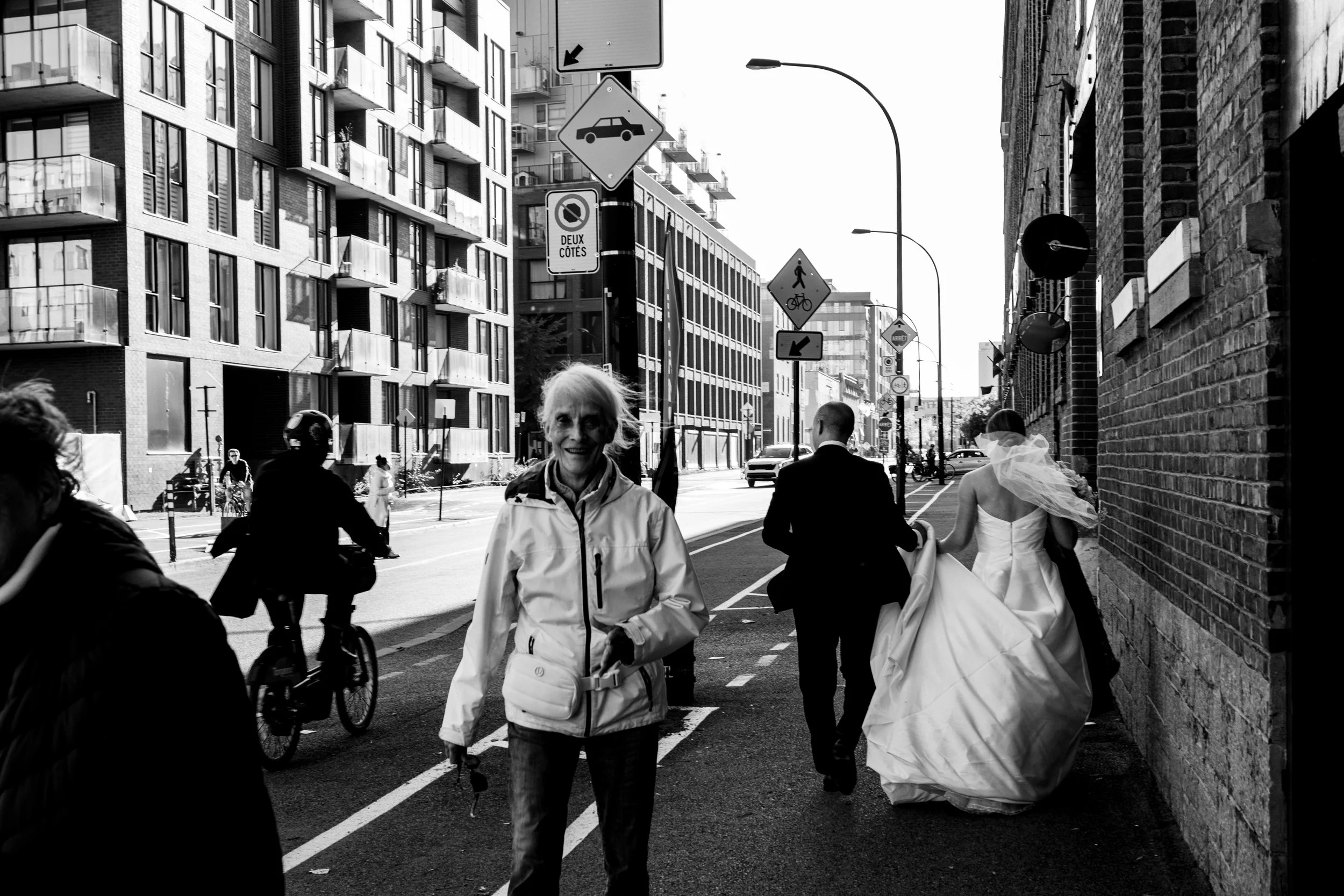 Black and white photograph of a bride and groom walking through the streets of Griffintown, Montreal, surrounded by pedestrians and cyclists.