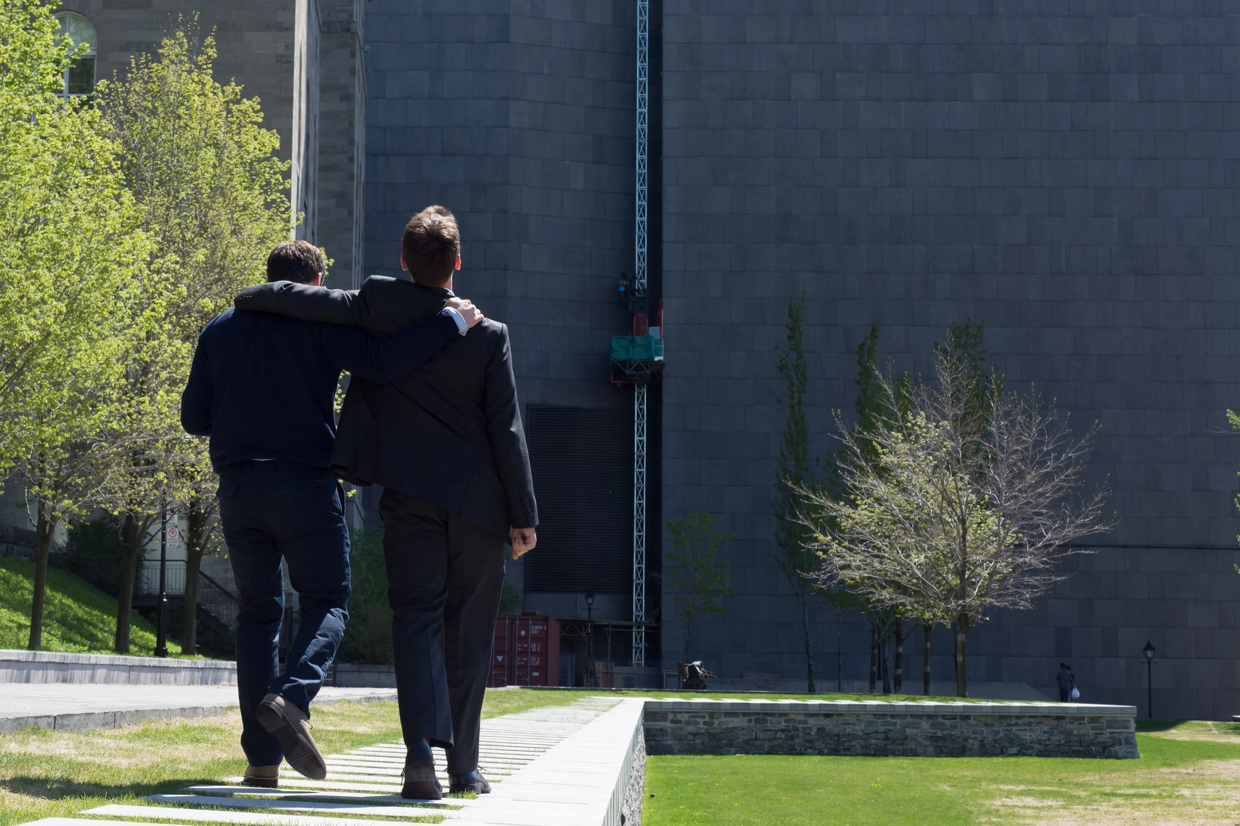 two men in navy suits holding shoulders walking away from camera