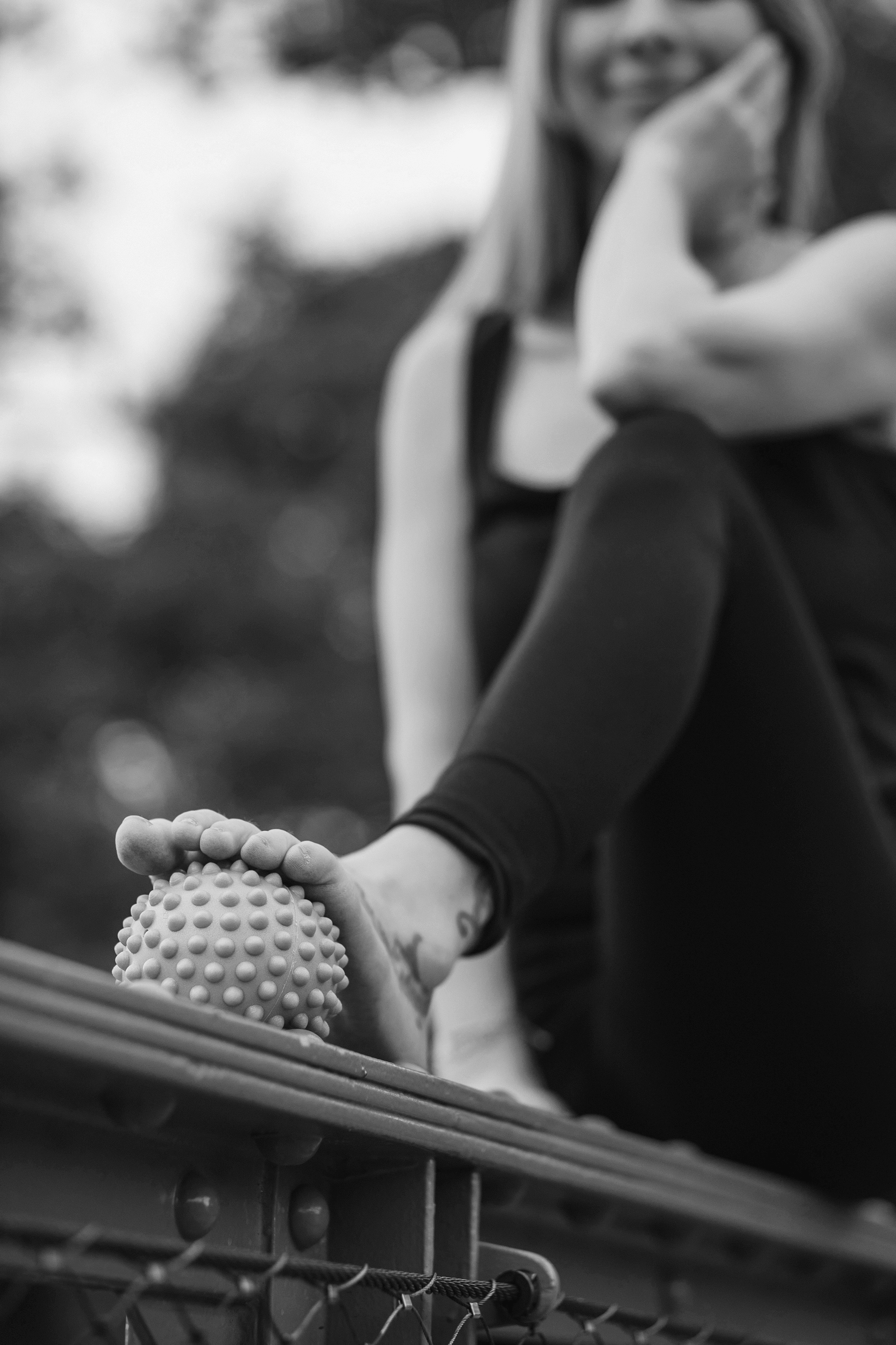 Nahaufnahme einer Person, die auf einer Balanceübung sitzt, mit einem Ball mit Noppen, auf einem Spielplatz oder in einem Fitnessbereich, im Hintergrund unscharf.
