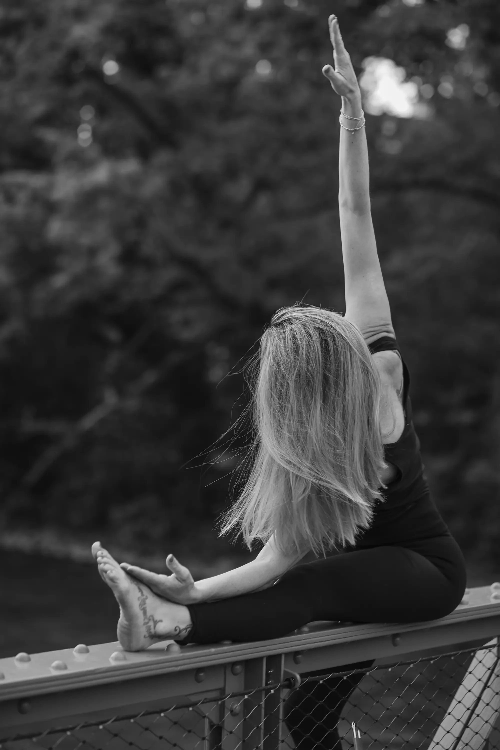 Eine Frau macht Yoga im Freien, sitzt in der Haltung des Lotus, mit einer Person im Hintergrund, die sich ebenfalls streckt.