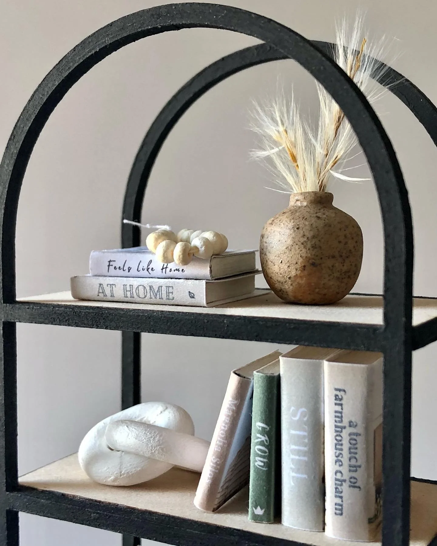 Decorative shelf with books, a ceramic vase with dried grasses, a white stone sculpture, and a shell.
