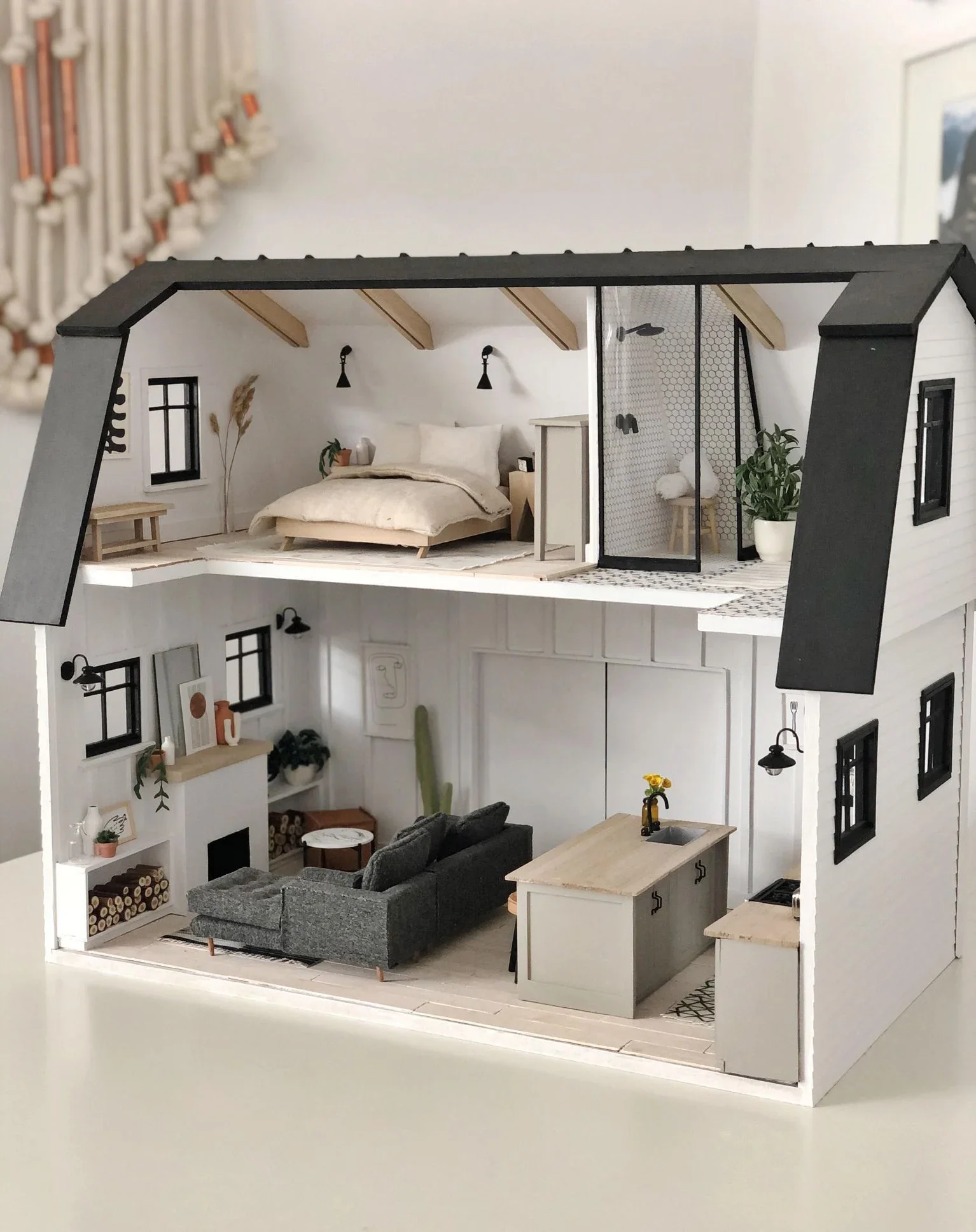 Miniature dollhouse with two floors, showing a bedroom with a bed, nightstand, and window on the upper floor, and a living room with a sofa, coffee table, and fireplace on the lower floor.