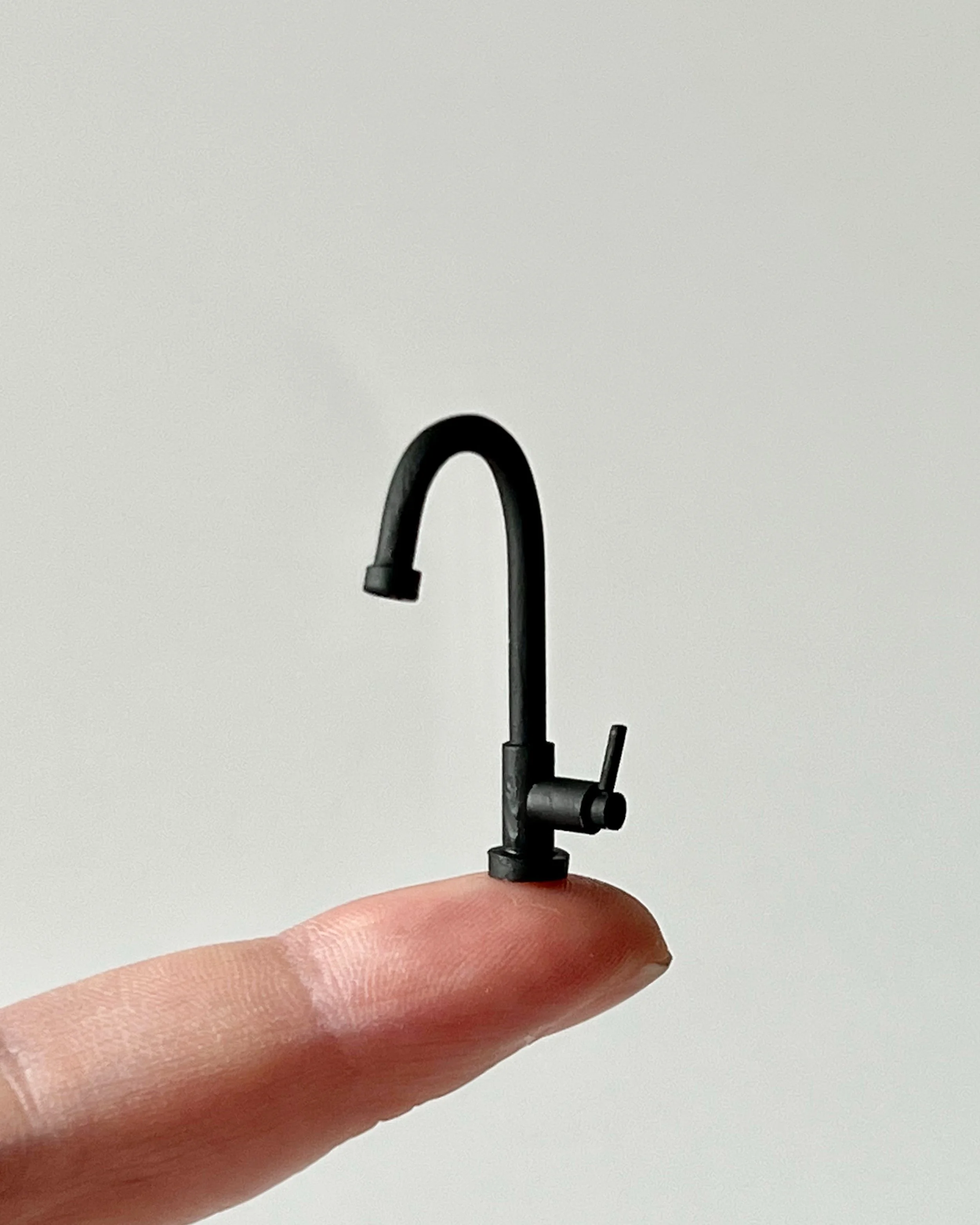 A small black faucet held on a finger against a plain gray background.
