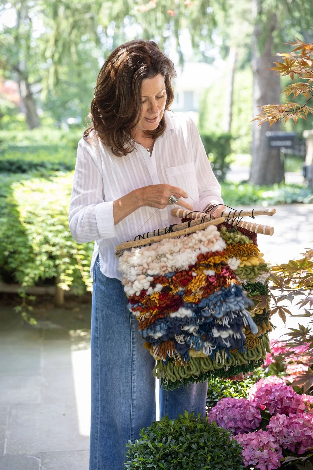 A woman looking at a basket of hand-spun yarn outdoors, surrounded by greenery and pink hydrangeas.