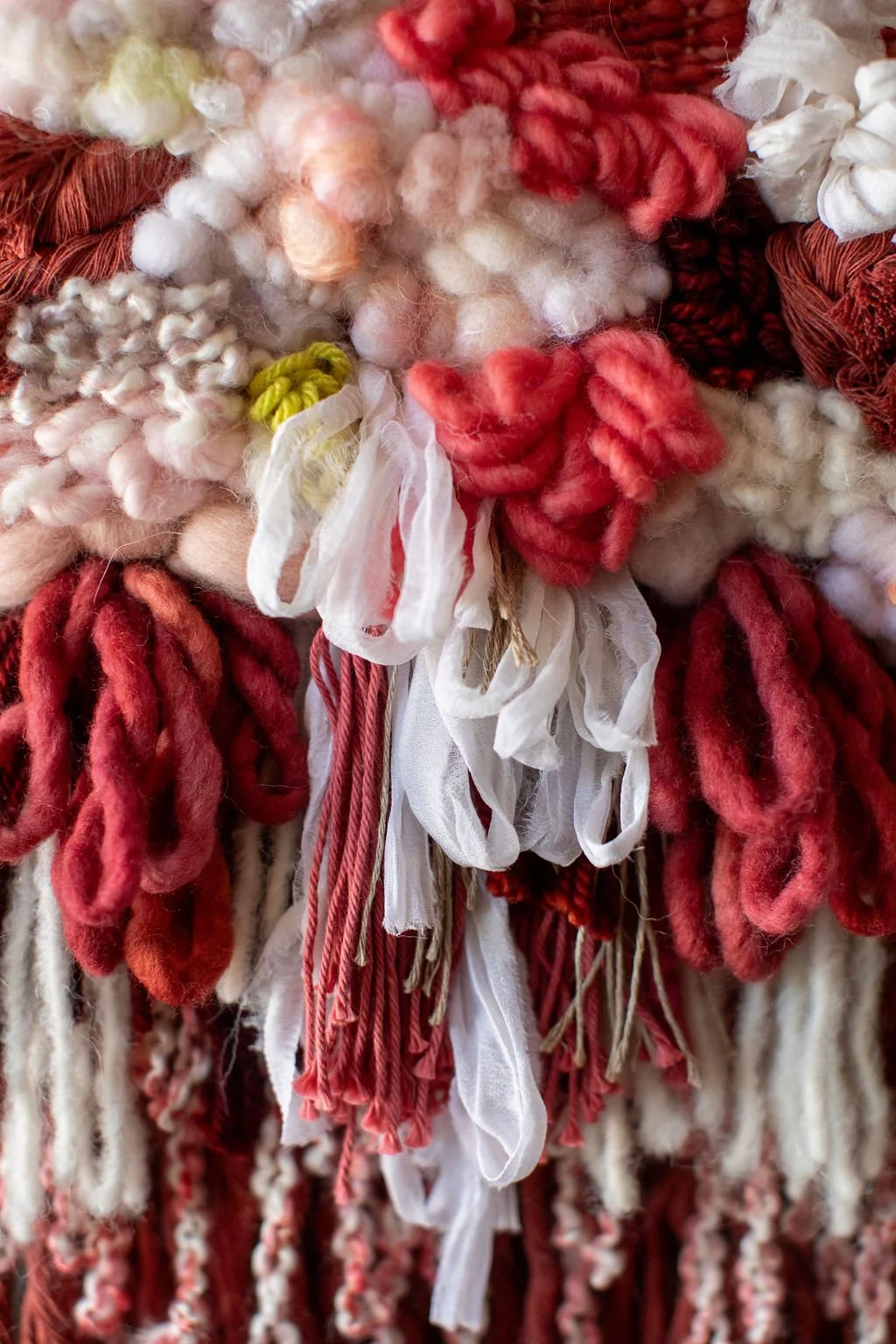 Close-up of various colorful yarns and textiles, including shades of red, white, pink, and yellow, with different textures and thicknesses, arranged in a decorative manner.