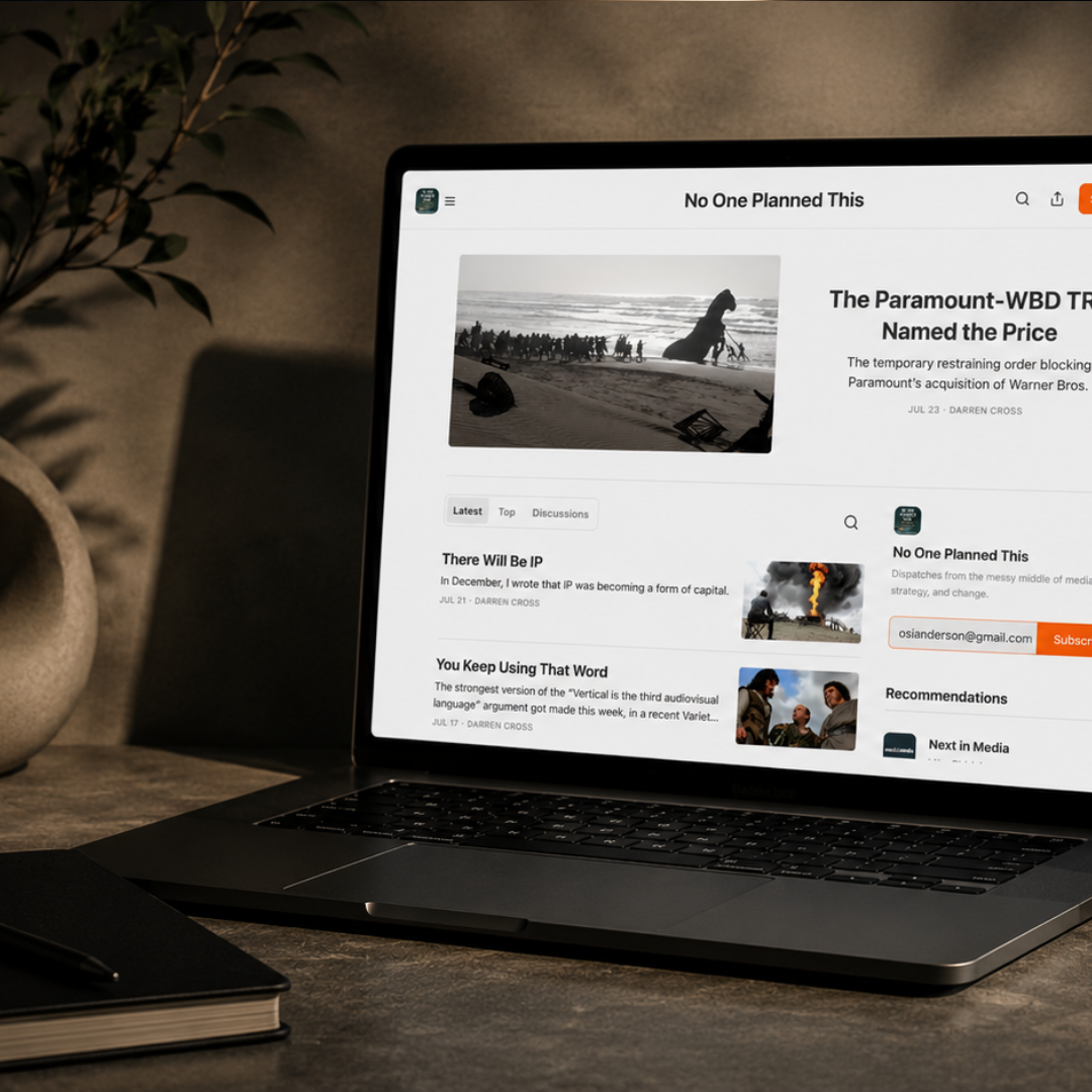 Laptop displaying an entertainment industry news website featuring articles about film, television, and media, photographed on a modern desk beside a notebook and plant.