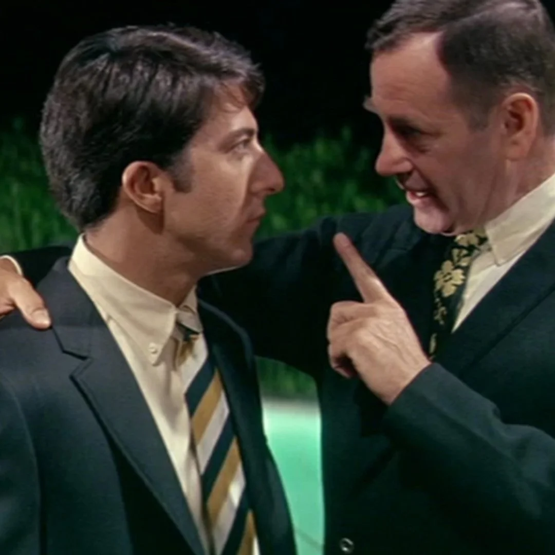 Two men in suits share an intense face-to-face conversation, with one pointing a finger while speaking, capturing a tense dramatic moment.