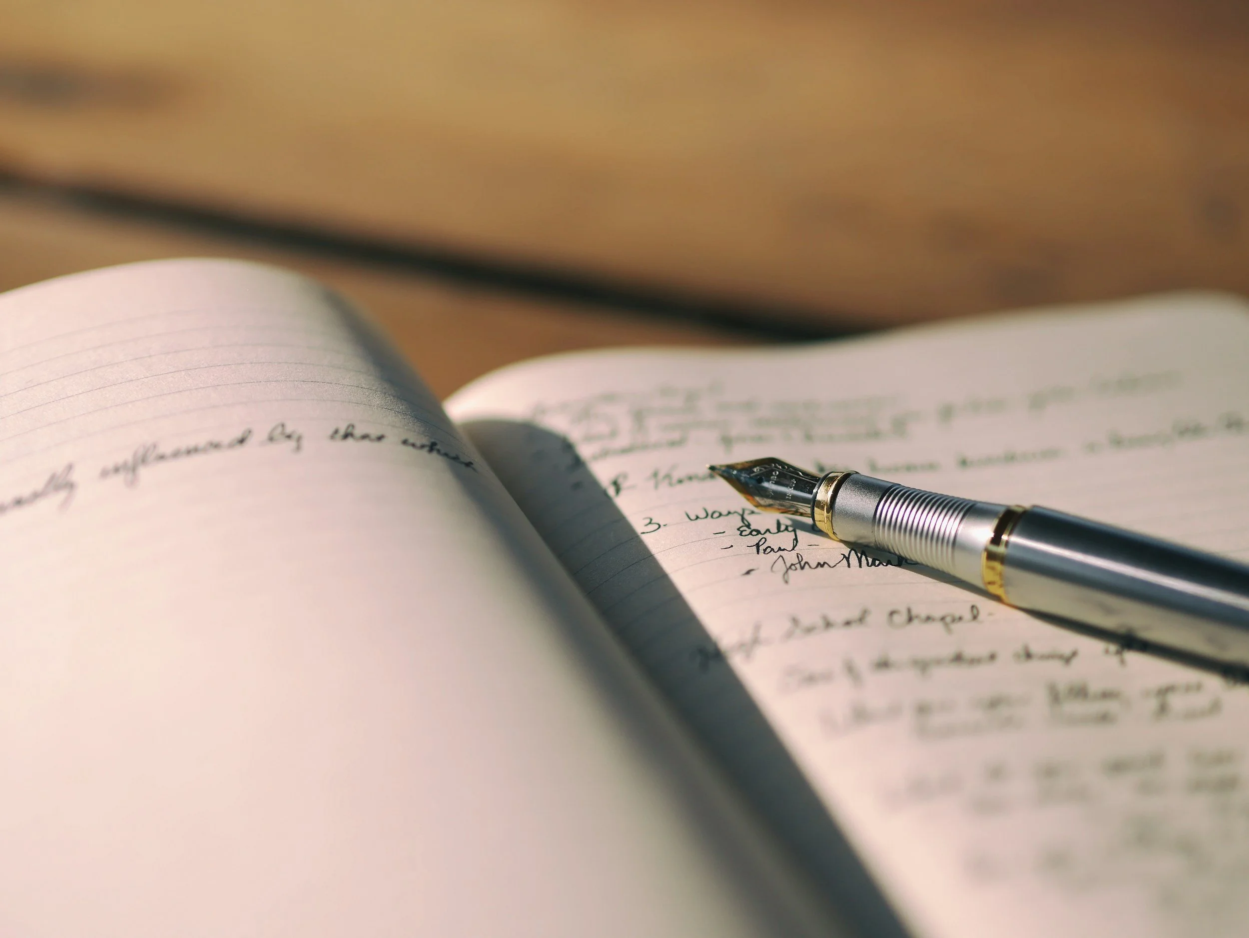 Close up of a fountain pen on an open, lined notebook with some handwritten words