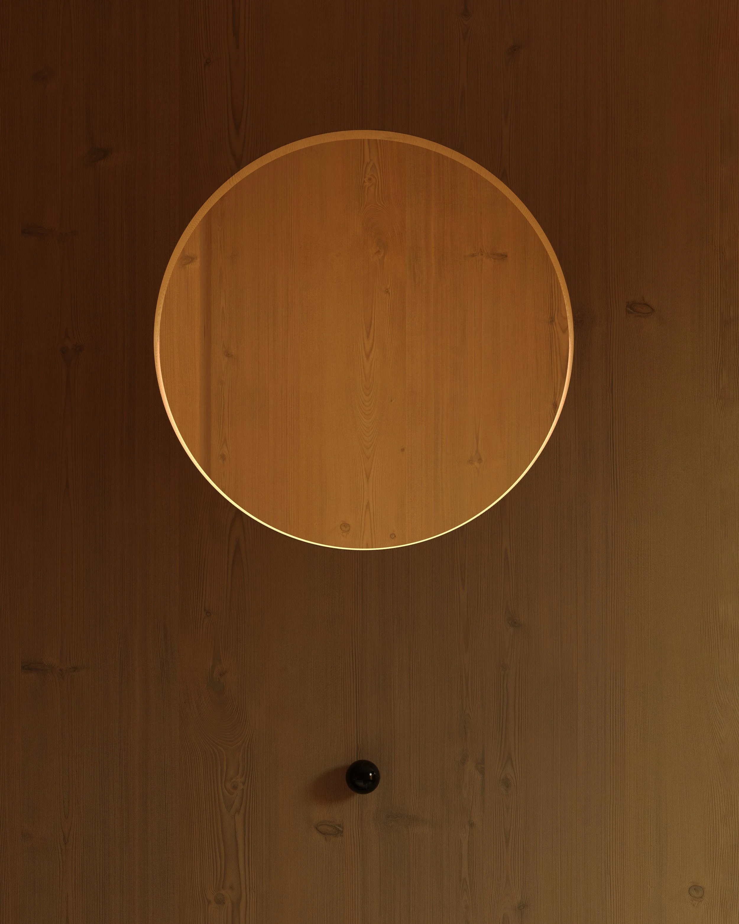 A wooden circular table on a wood floor with a black object at the bottom of the image.