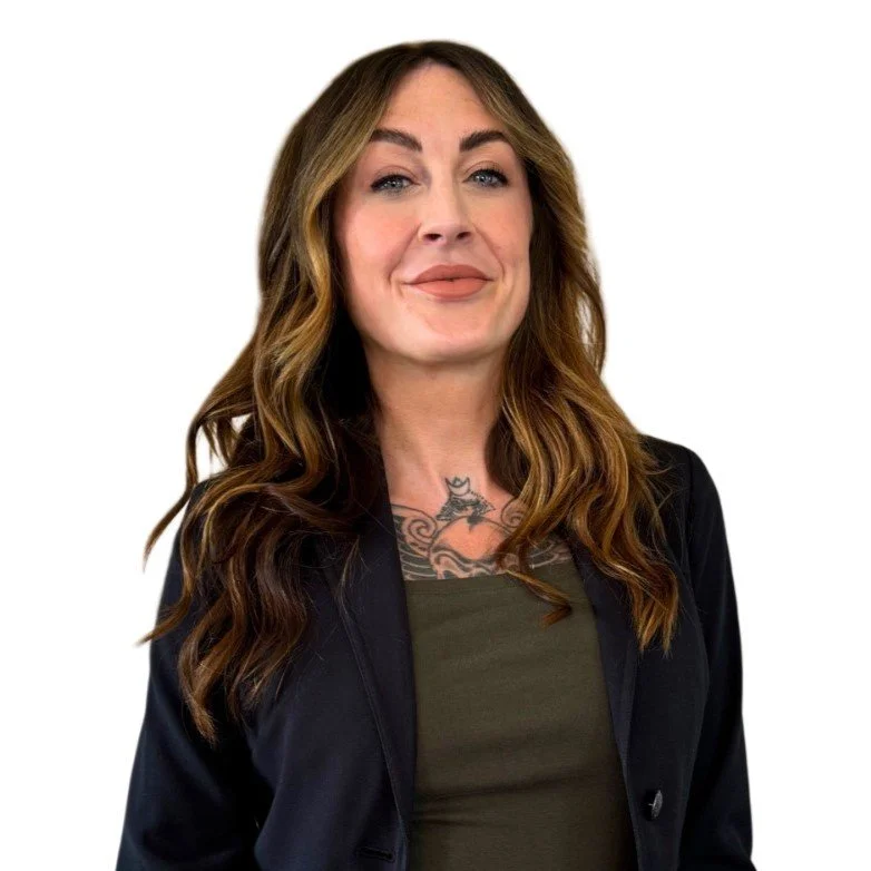 A woman with wavy brown hair, wearing a black jacket over an olive green top, smiling with a confident expression, against a plain white background.