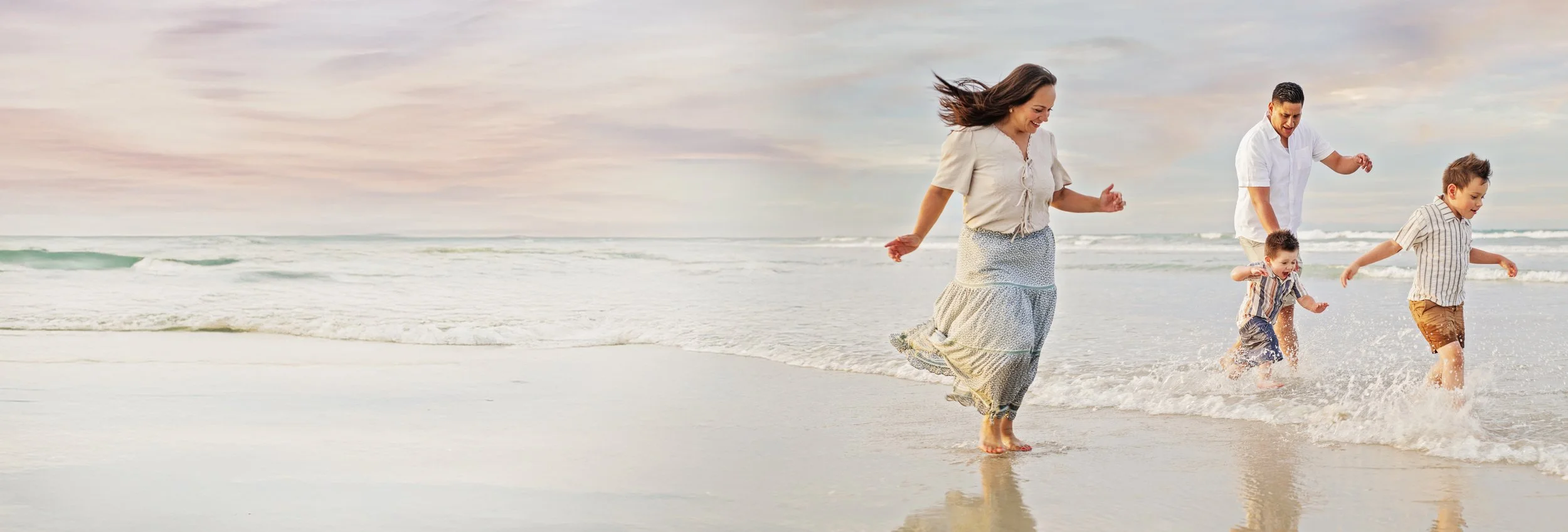 Family of four, mom, dad and two small boys running in the ocean at New Smyrna Beach during a photoshoot