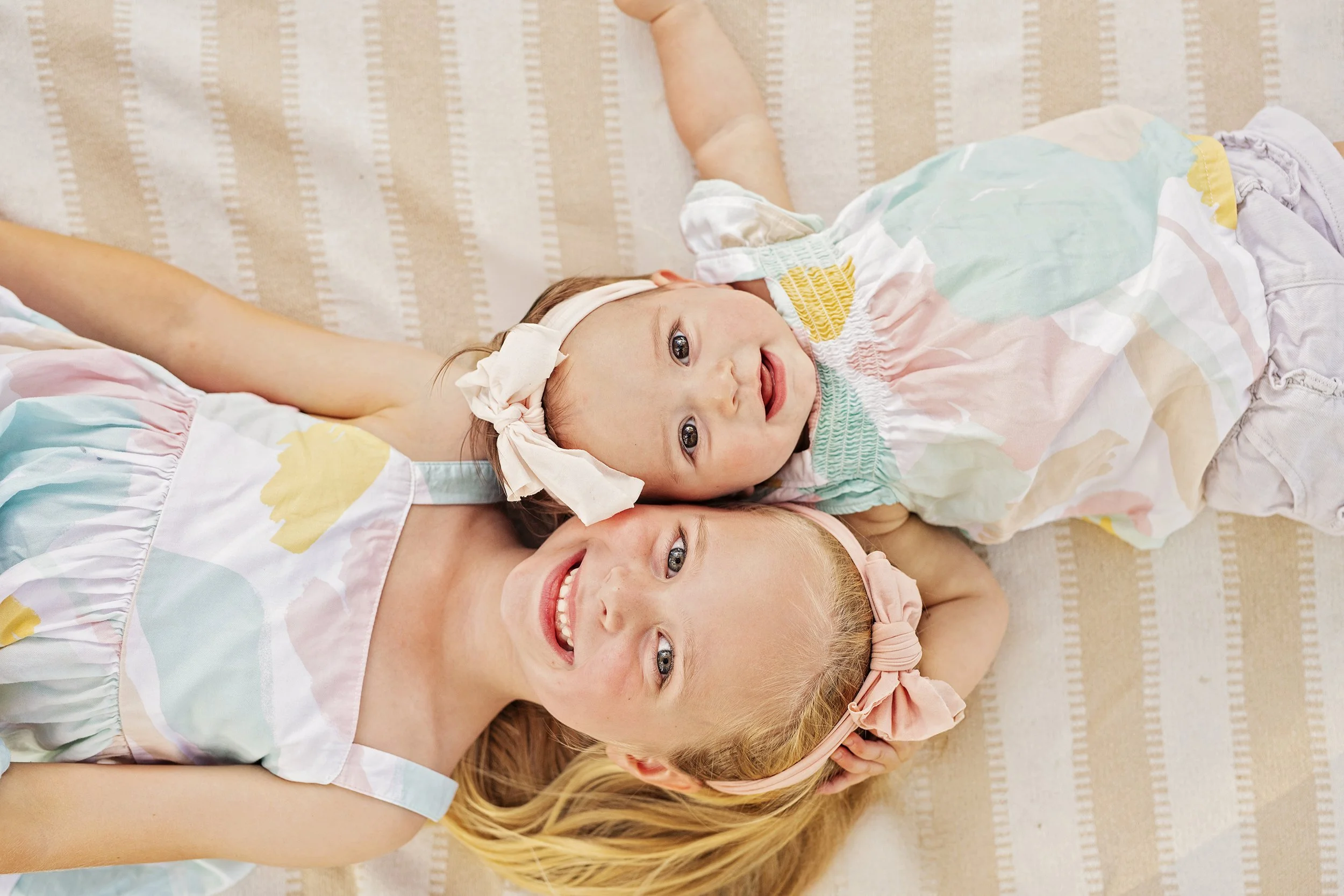 Two sisters laying on a blanket taking a photograph with big smiles