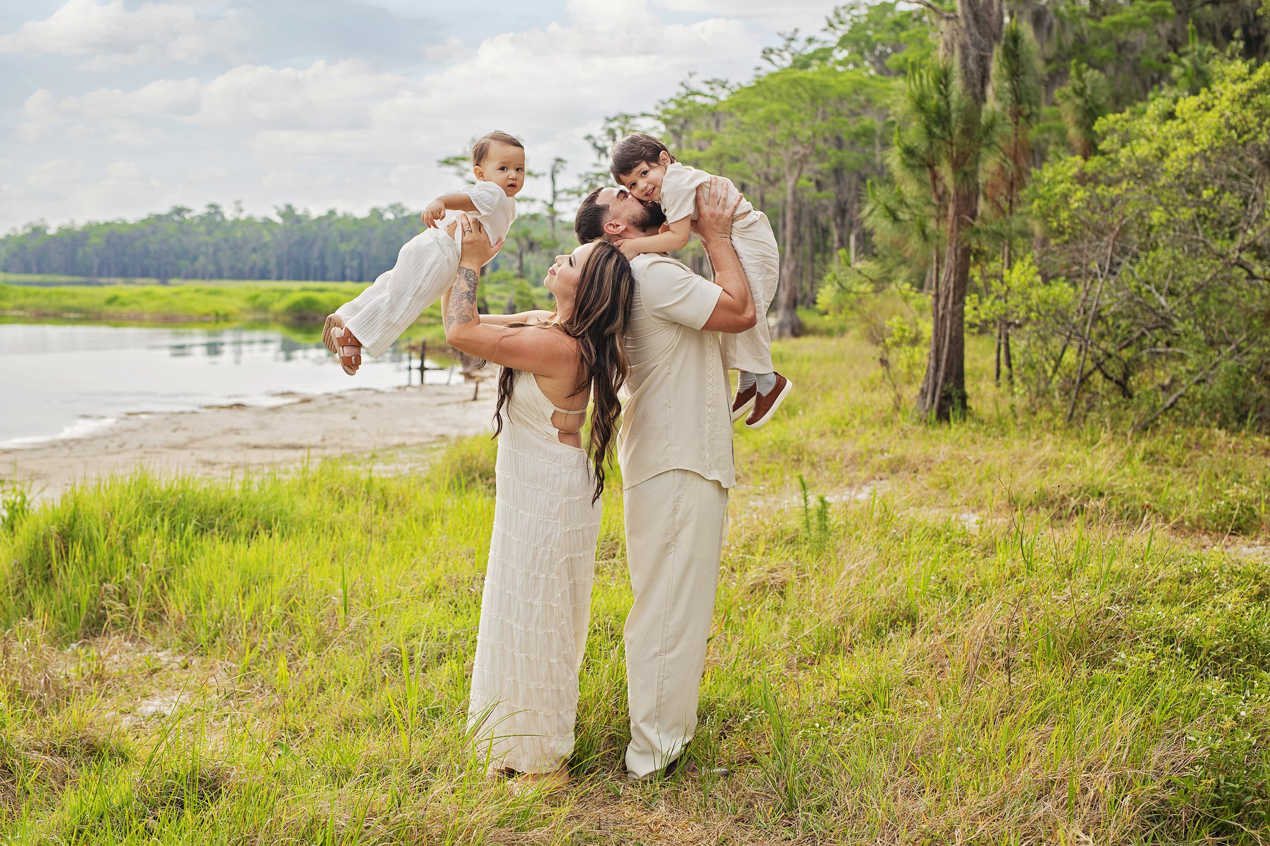 Family of 4 with 2 young boys, mom and dad are holding the boys in the air with a beautiful background in Central Florida