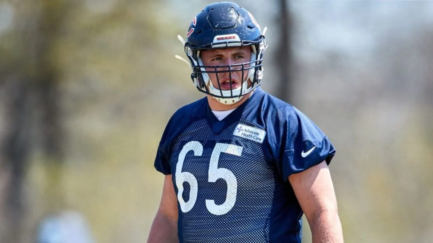 A male football player wearing a navy blue helmet and jersey with the number 65 on it, standing outdoors.