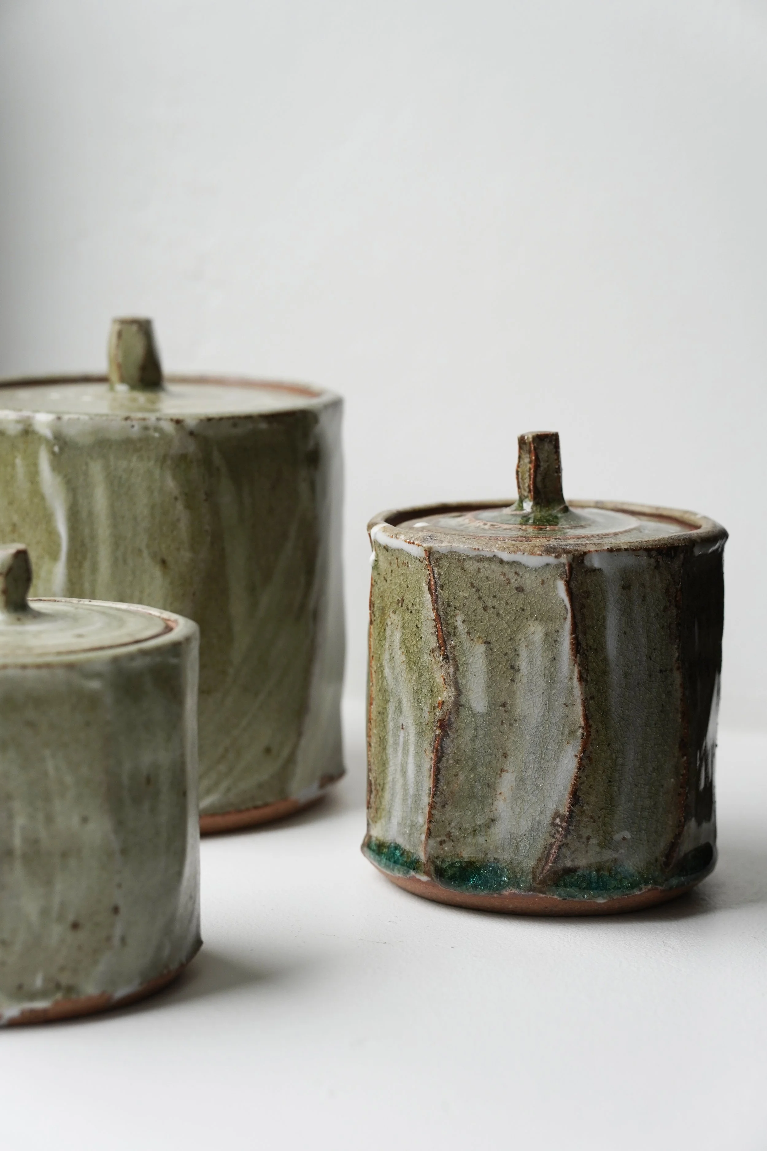 Three small handcrafted ceramic vases with a square shape and rounded edges, glazed in earthy tones, on a white surface against a plain white background.