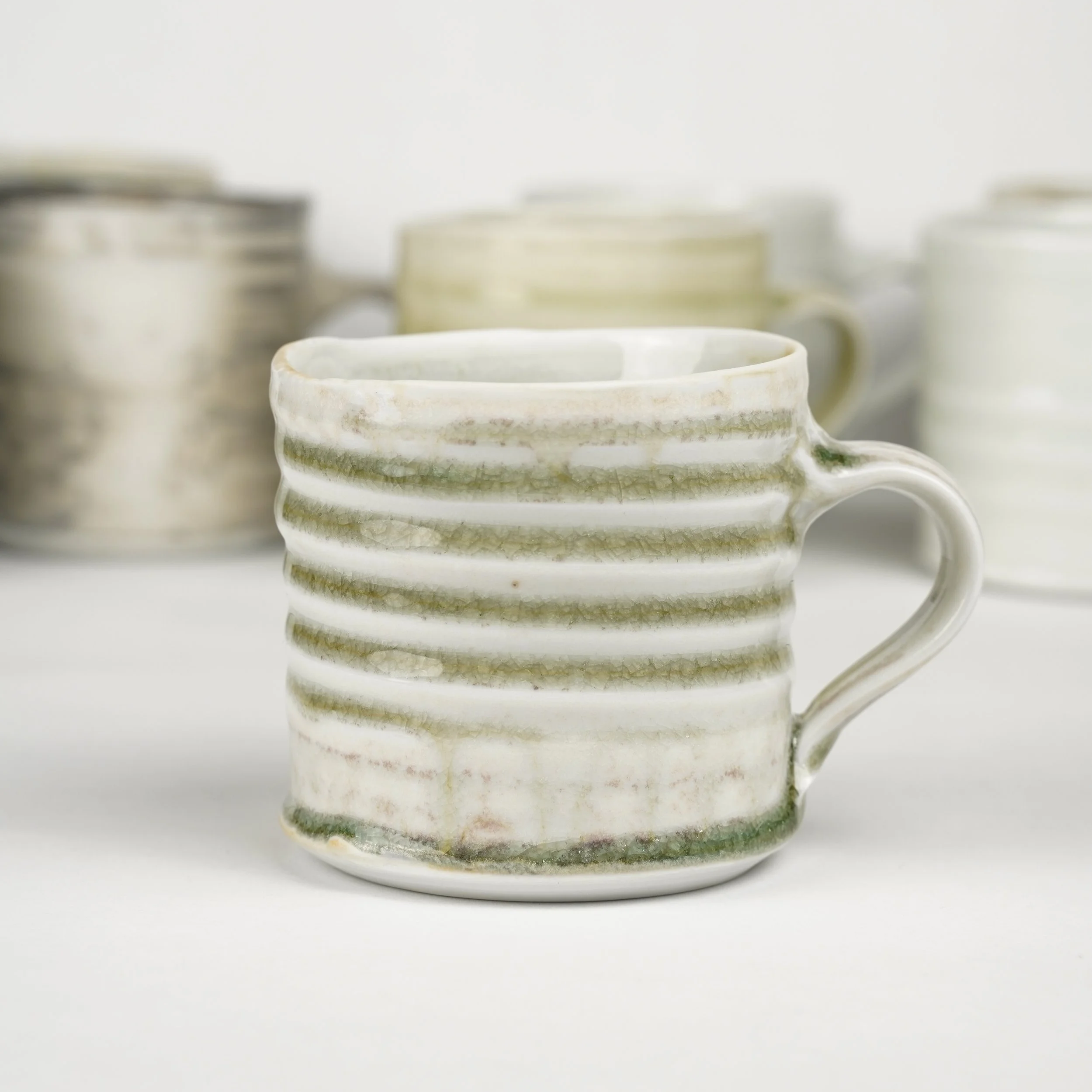 Close-up of stacked ceramic cups with green decorative accents on a white background.