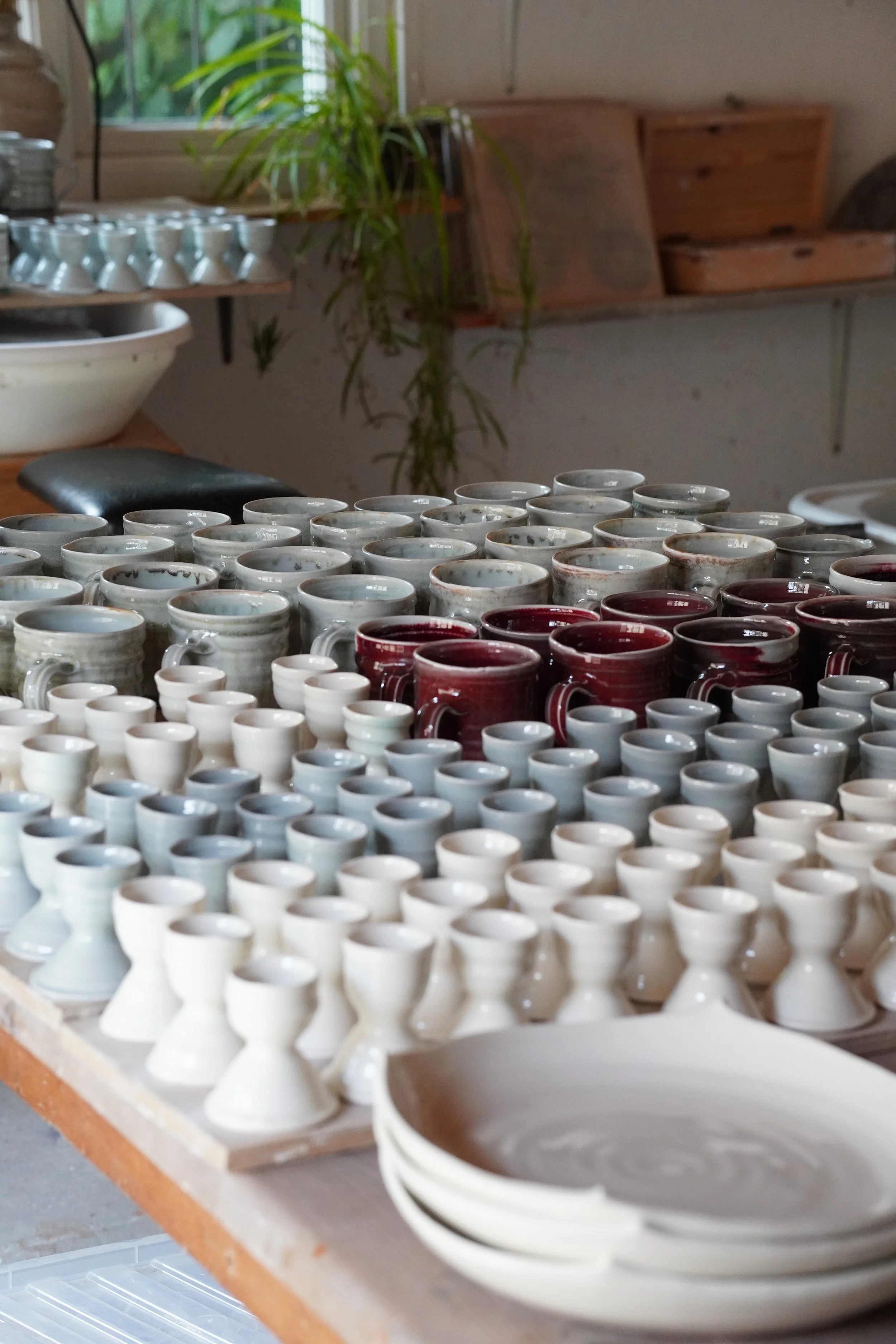 Various finished ceramic cups and bowls on a wooden table in a pottery studio.
