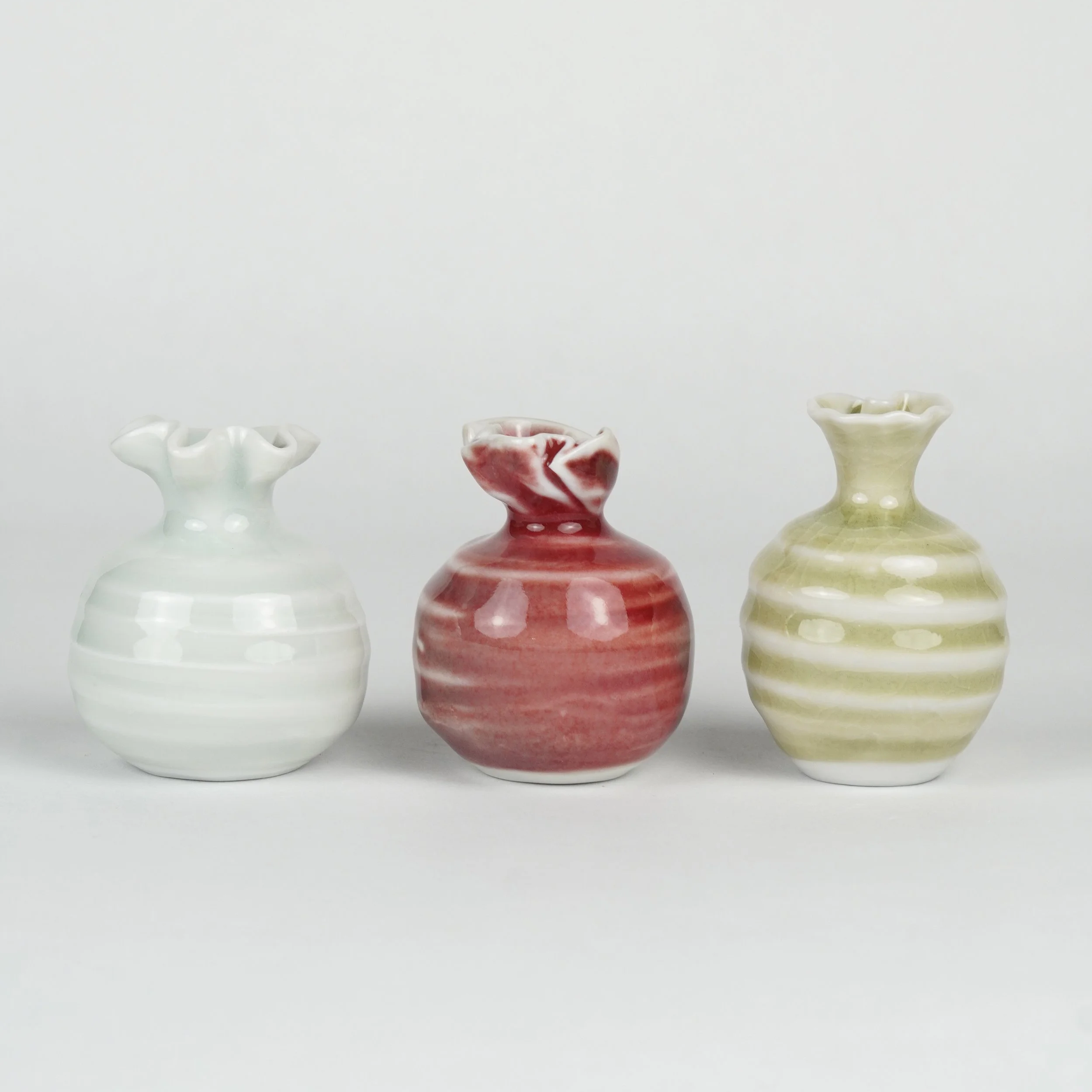 Four decorative porcelain vases with ruffled edges, in white and pinkish-red colors, arranged in a row against a plain light background.