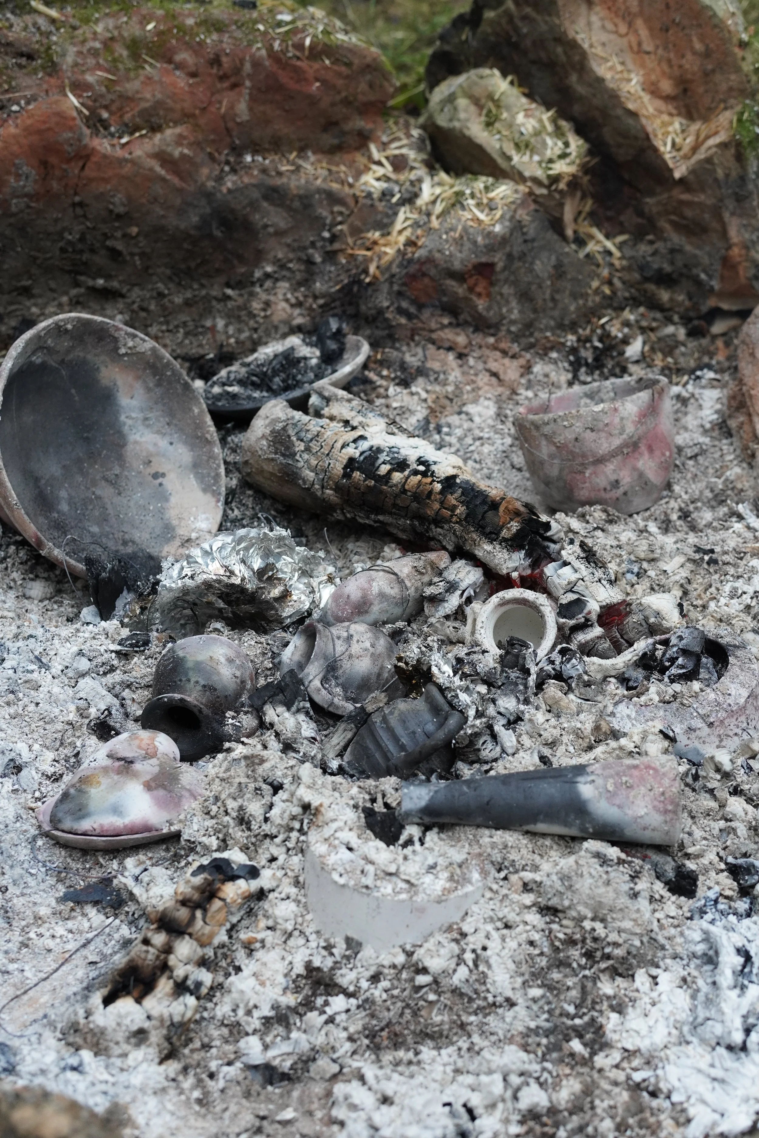 Ashes, burnt pottery, and charred debris on a firepit or outdoor fire area.