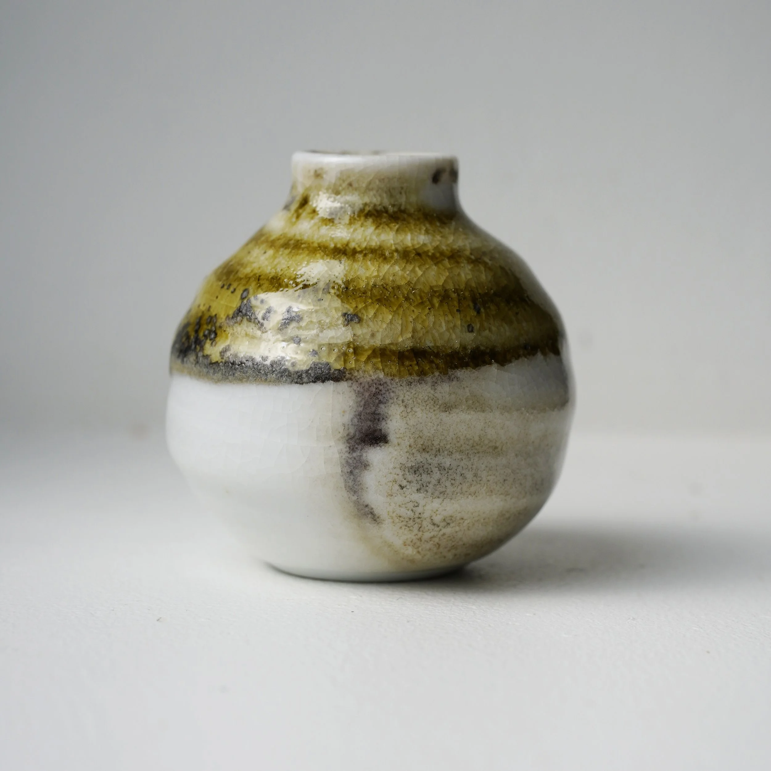 Close-up of a ceramic vase with a beige and brown textured pattern, placed on a white surface with a plain light gray background.