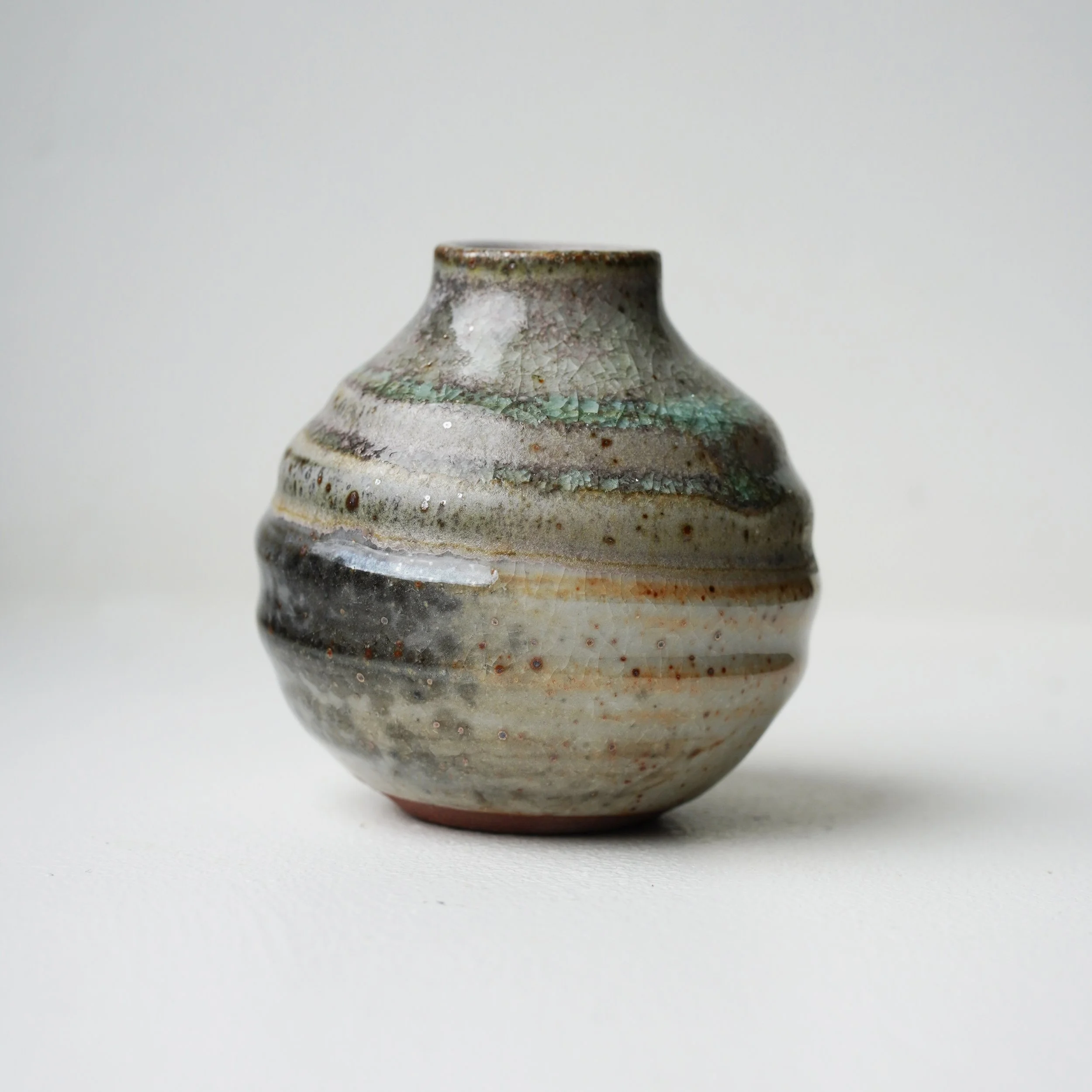 Close-up of a textured ceramic vase with earthy tones against a plain, light background.