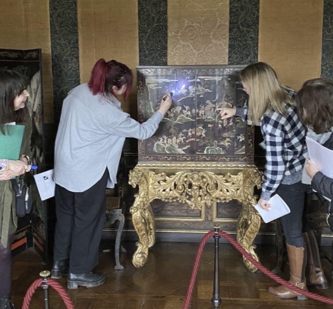 Group of four women observing and pointing at an ornate, historic painted cabinet in a museum exhibit.