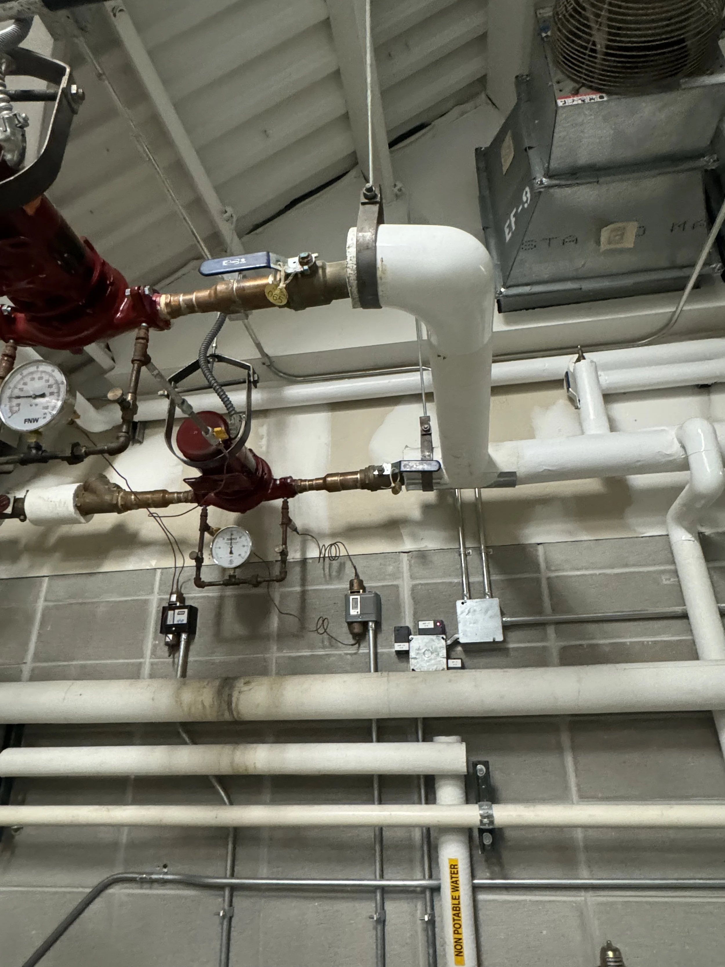 Ceiling with various pipes, gauges, electrical boxes, and an air conditioning unit. Maintnance closet. BTI Balance Technologies air and water balancing in Milwaukee.