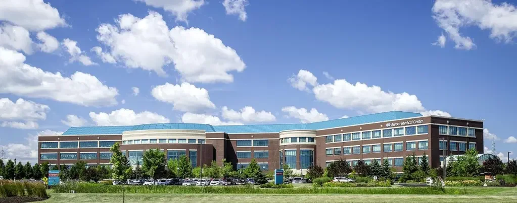 A large modern hospital building with a blue roof, lots of windows, and surrounding greenery, labeled Aurora Medical Center.