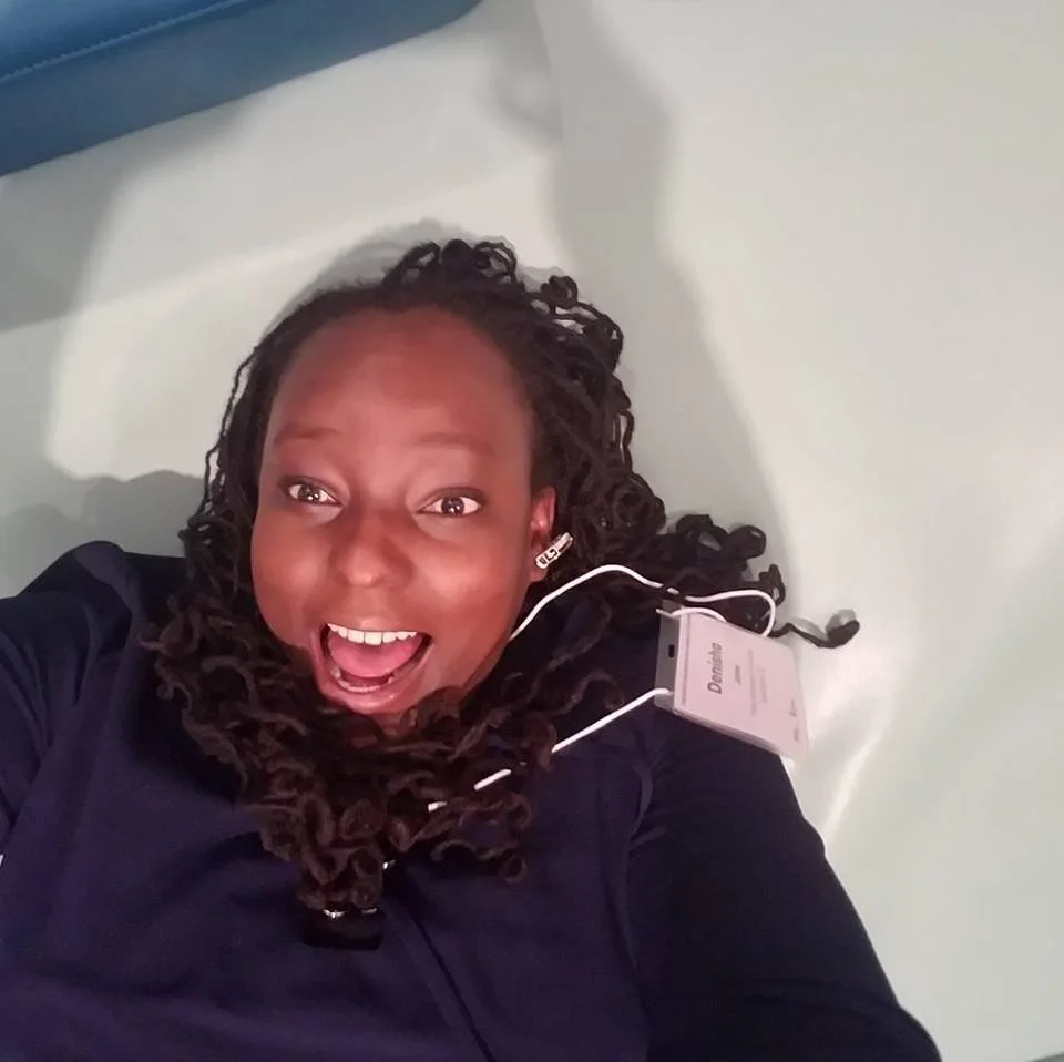Woman lying on a hospital bed, smiling, with a medical device or tag attached to her neck.