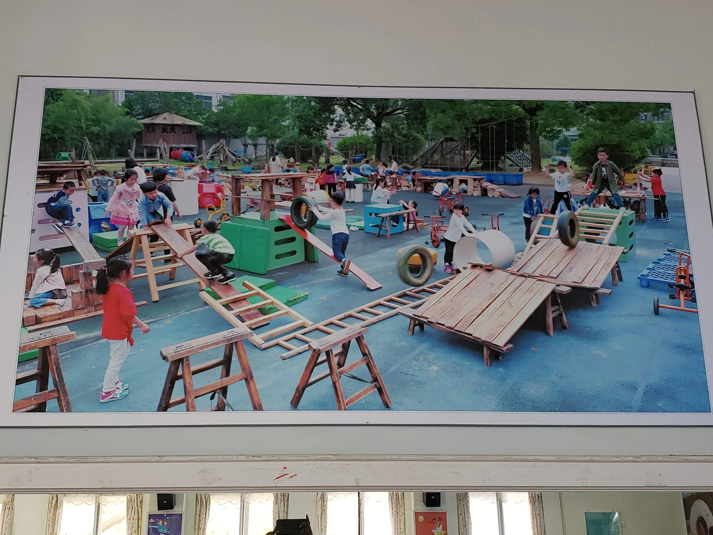 Children playing on wooden structures in an outdoor playground surrounded by green trees.