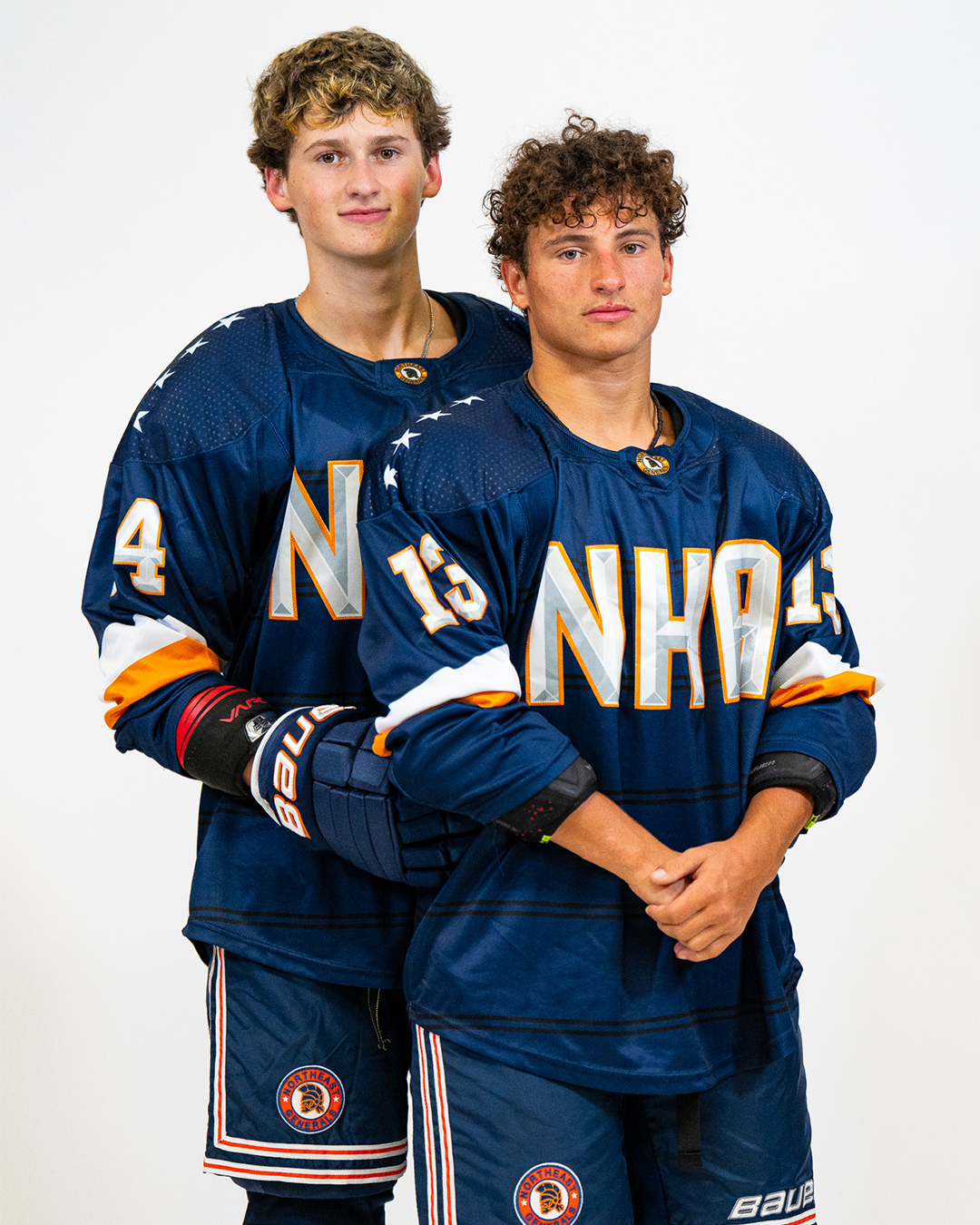 Two young male hockey players in blue jerseys with 'NHA' logo, standing against a plain white background.