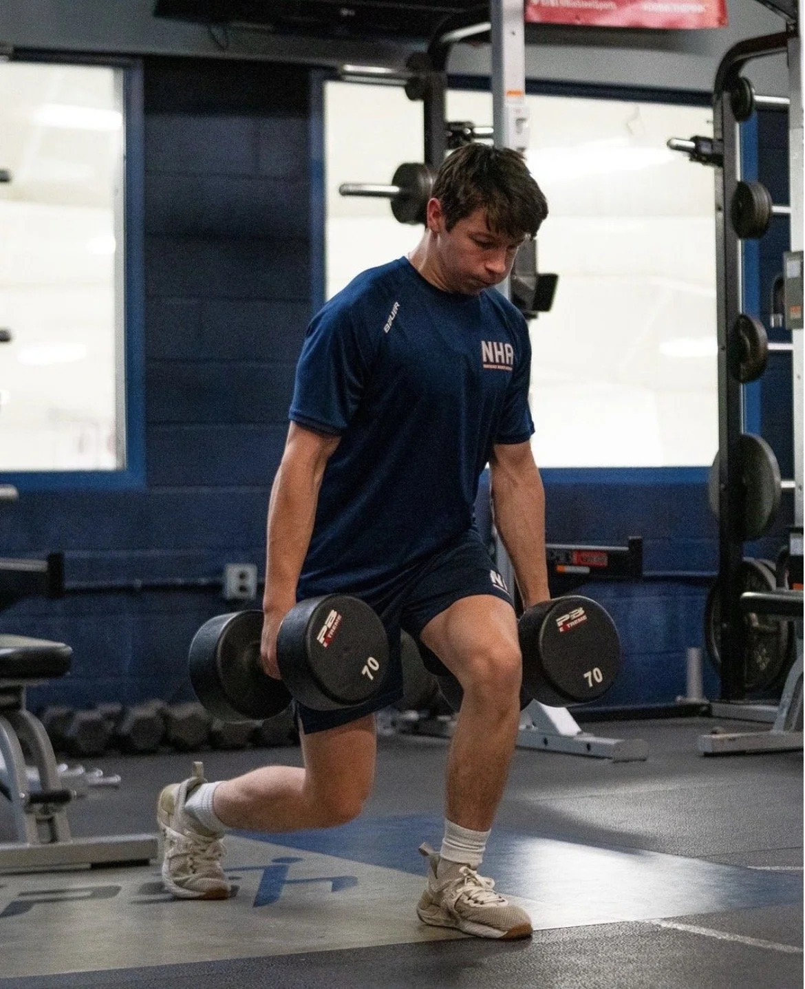 A man performing a lunge exercise with dumbbells in a gym.