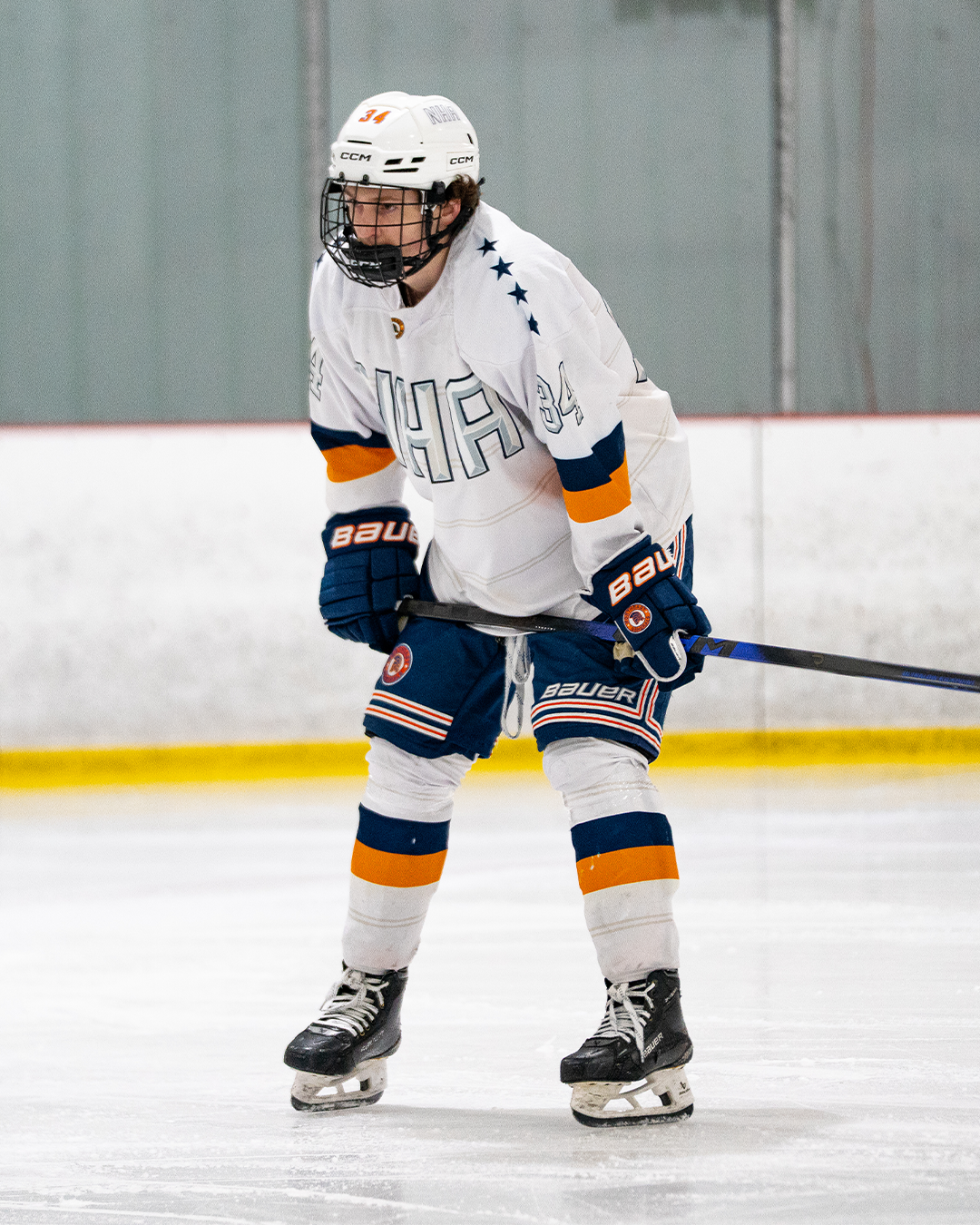 Hockey player in white jersey and blue pants on ice rink, wearing a helmet and holding a hockey stick.