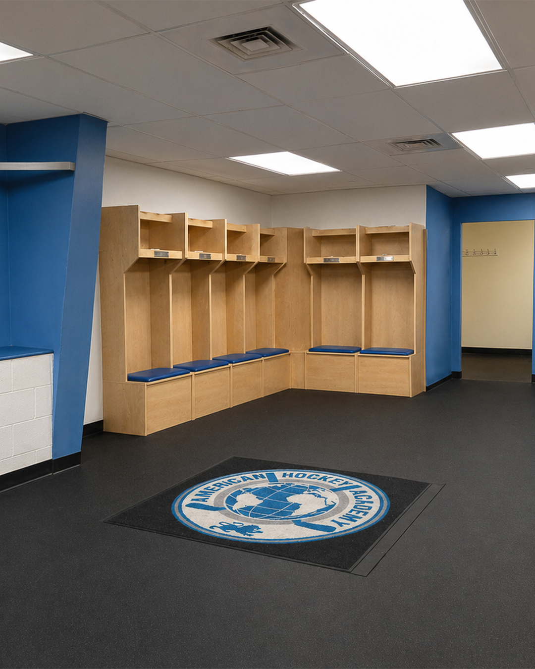 Locker room benches with blue cushions in a hockey team locker room, featuring a hockey team logo on the floor that reads 'American Hockey Conference' surrounding a globe and hockey sticks.