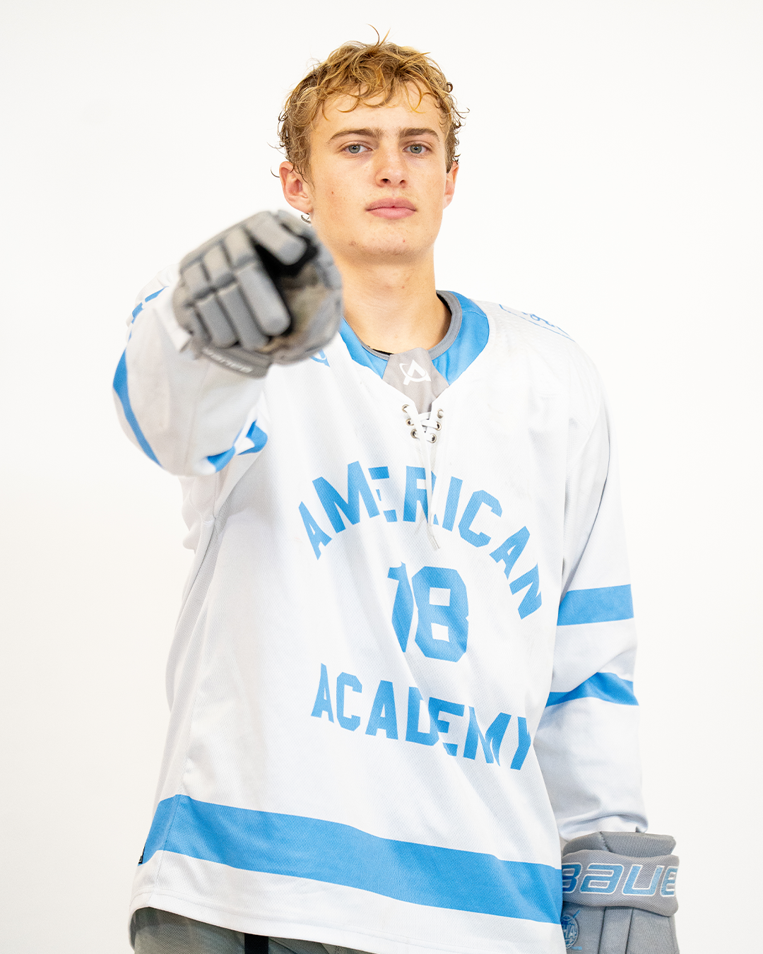 A young man wearing a white and blue hockey jersey pointing directly at the camera.