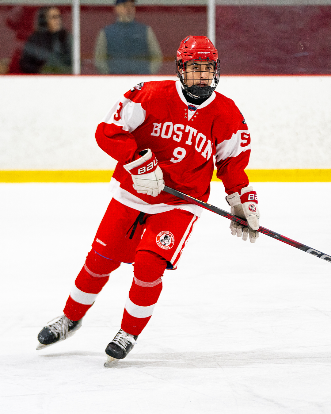 Hockey player in red Boston jersey number 9 skating on ice rink.