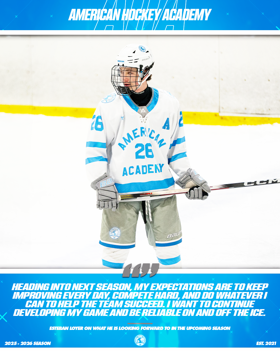 A young hockey player wearing a white jersey with blue accents, number 26, and an 'A' for assistant captain at American Hockey Academy, standing on the ice with a hockey stick, looking forward.