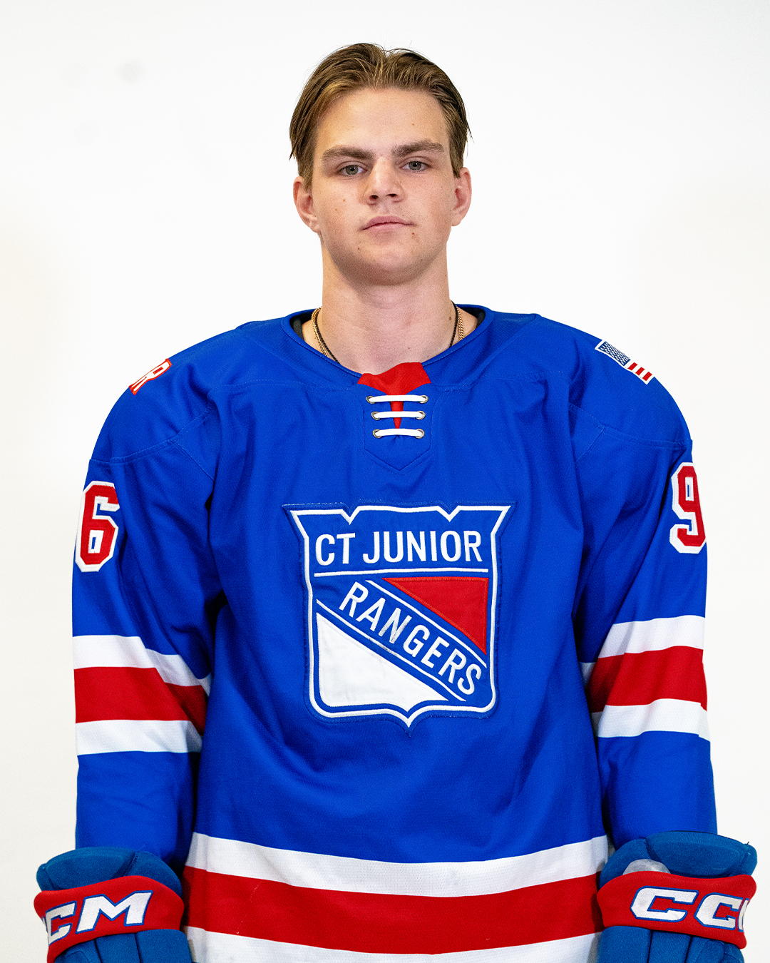 Young male ice hockey player wearing a blue jersey with red and white stripes, standing against a white background.