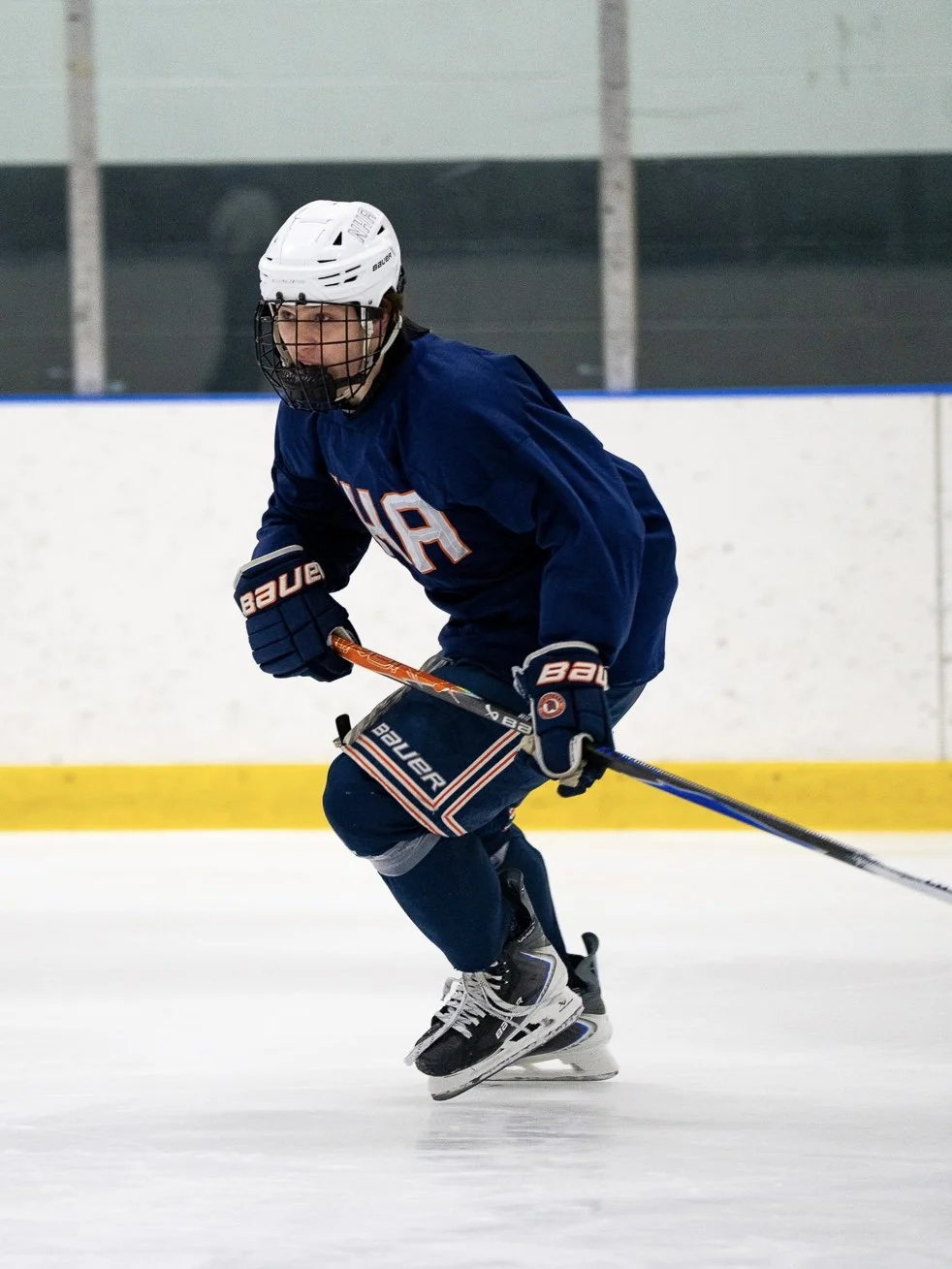 A person playing ice hockey on the ice rink, wearing a white helmet, blue jersey, and black skates.