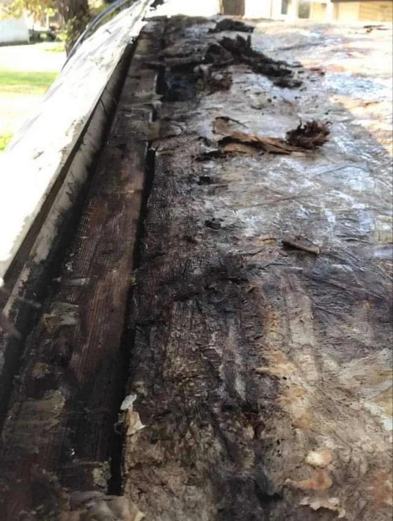 Burnt and charred wooden surface, possibly part of a burnt structure or debris, with some scattered remnants of burnt material and debris on top.